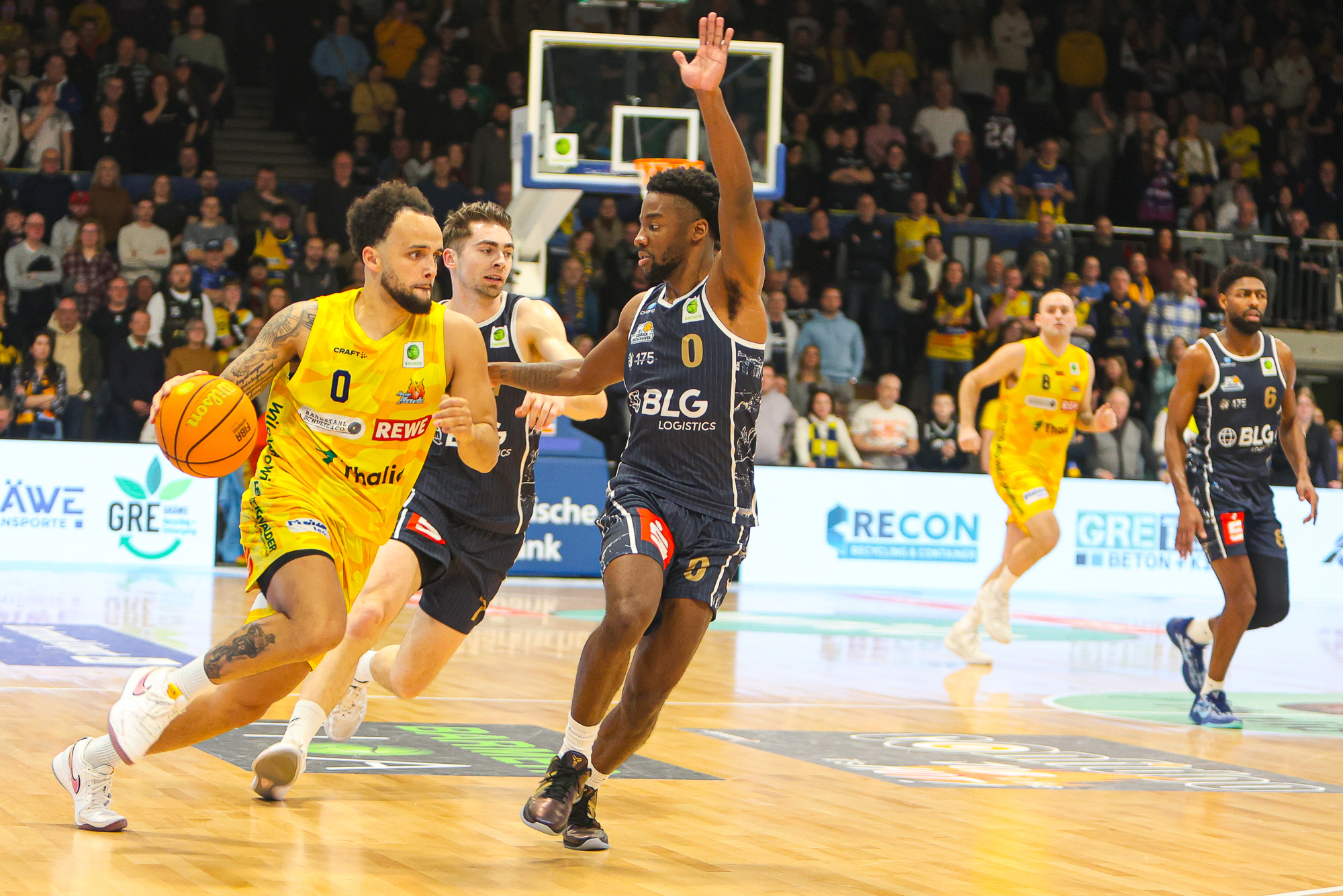 Ein Basketballspieler im gelben Trikot dribbelt dynamisch am Gegner im dunklen Trikot vorbei