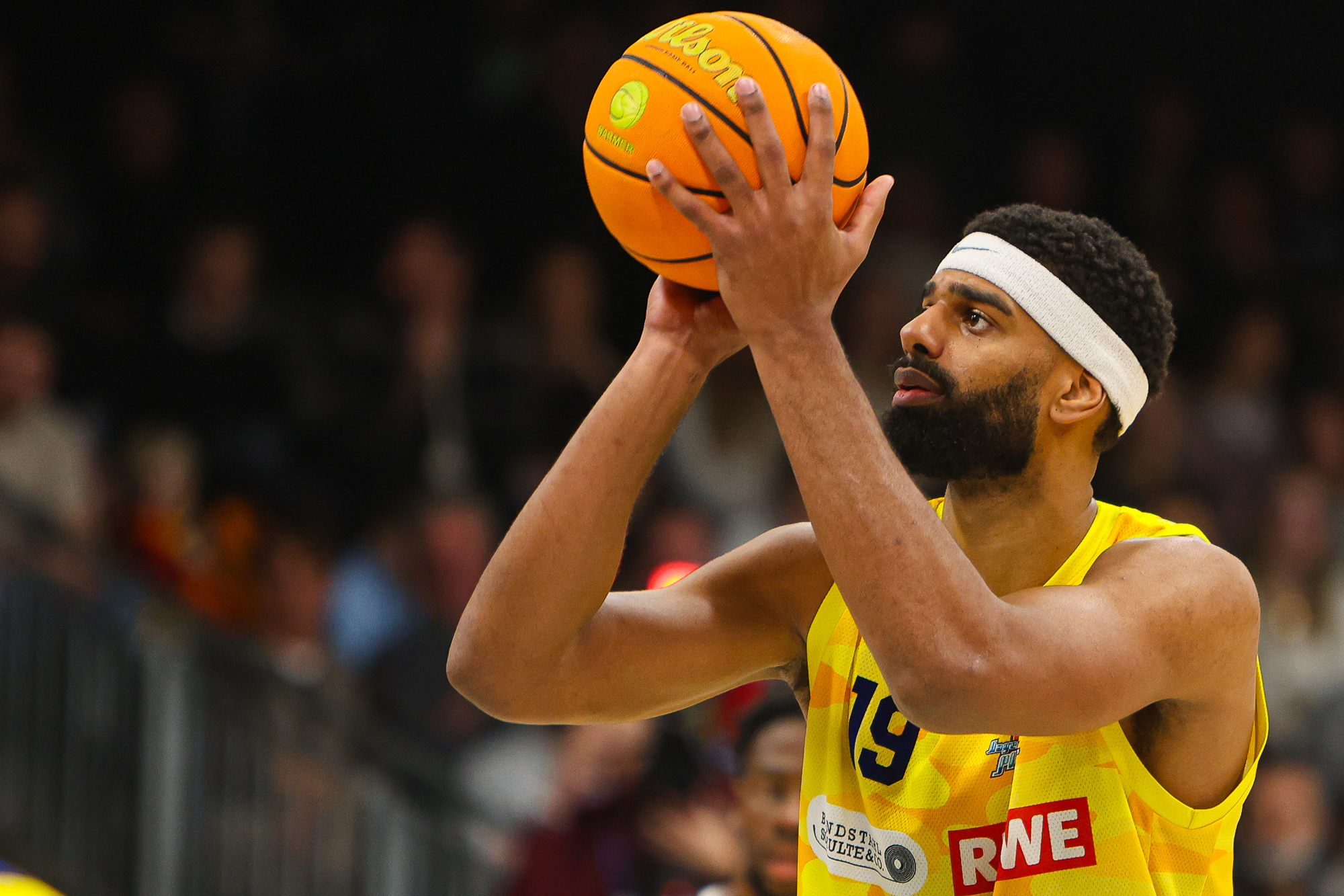 Ein Basketballspieler im gelben Trikot hält konzentriert den orangefarbenen Ball