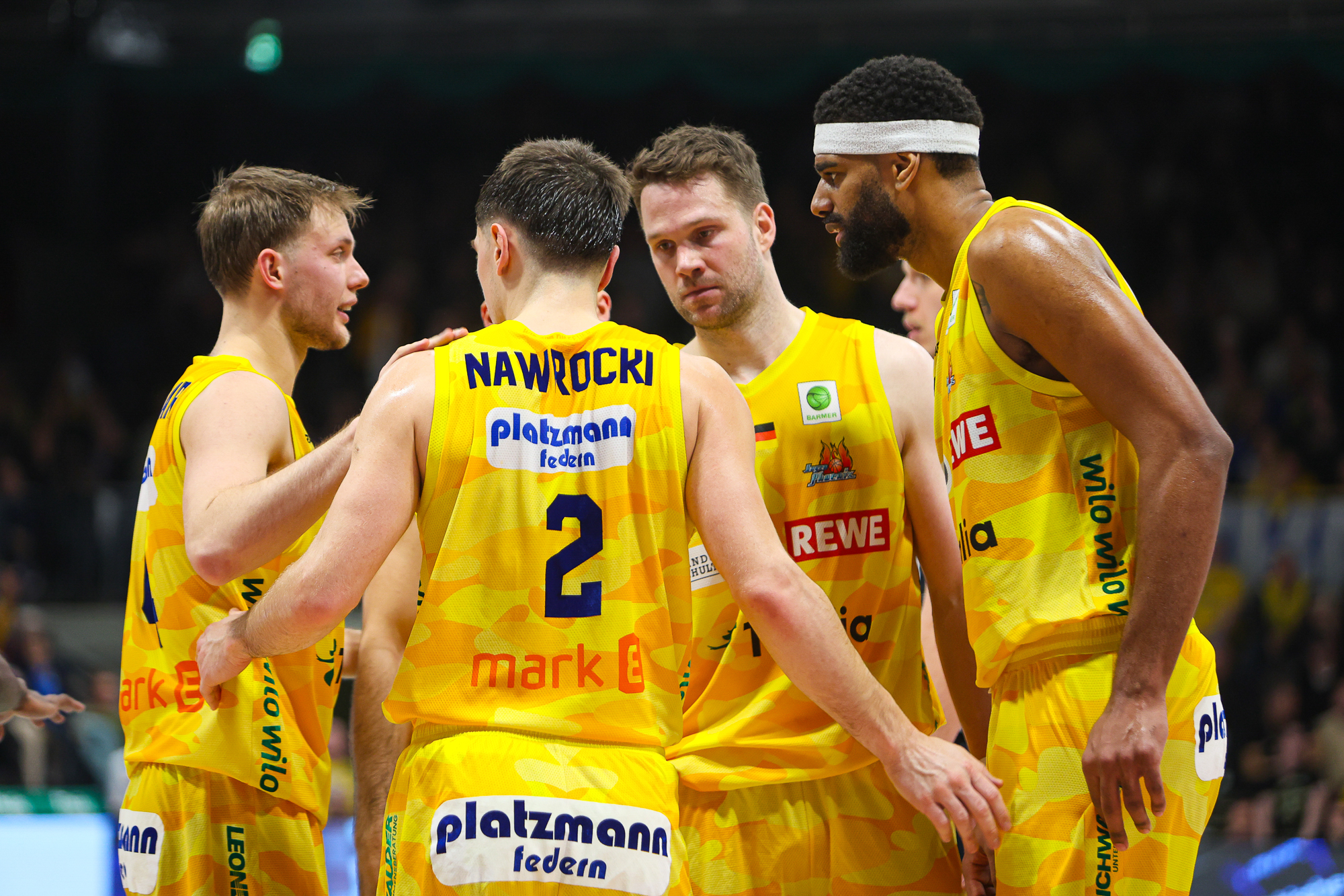 Vier Basketballspieler in gelben Trikots stehen zusammen, wirken konzentriert und engagiert