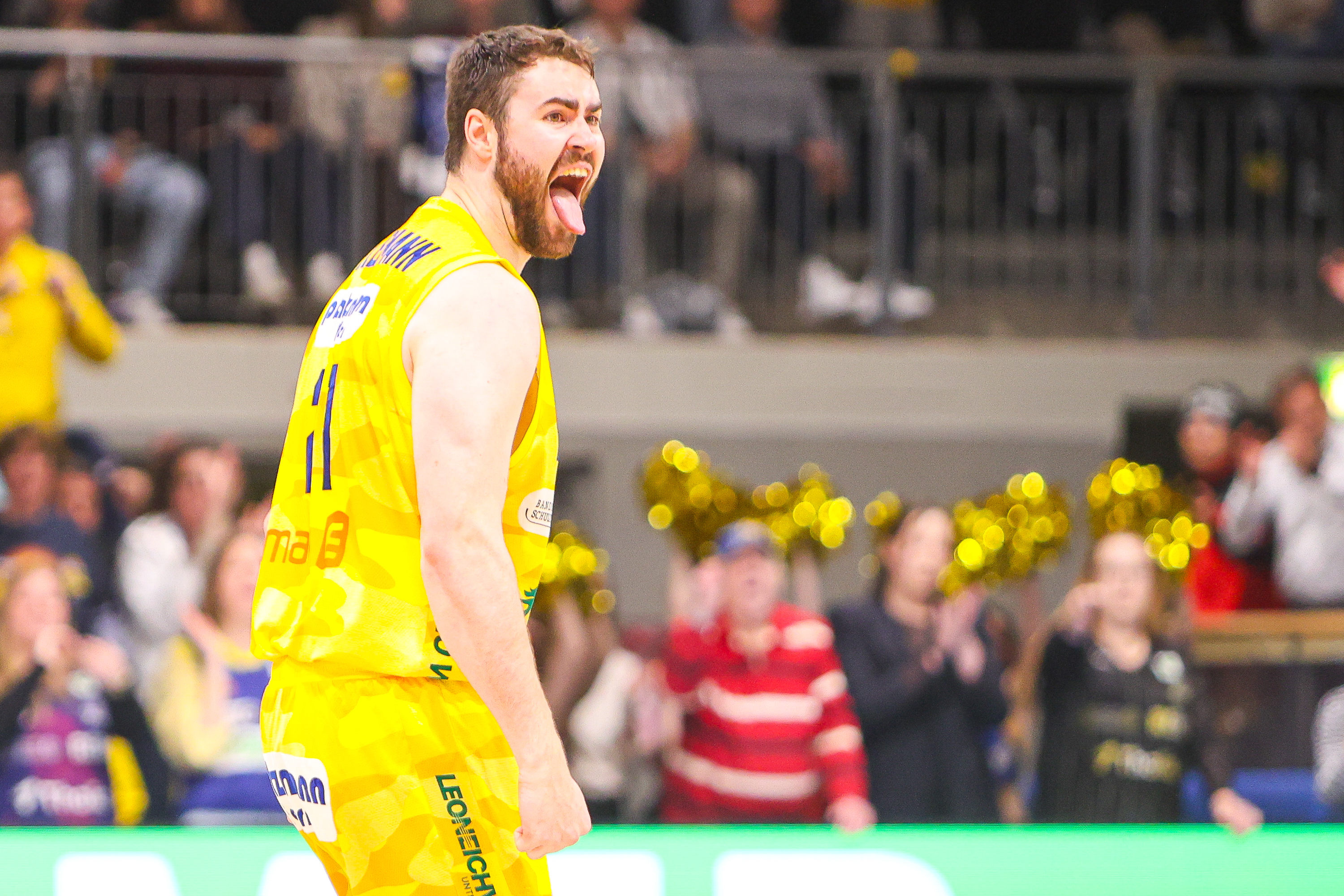 Ein Basketballspieler im gelben Trikot jubelt energisch mit offenem Mund auf dem Spielfeld