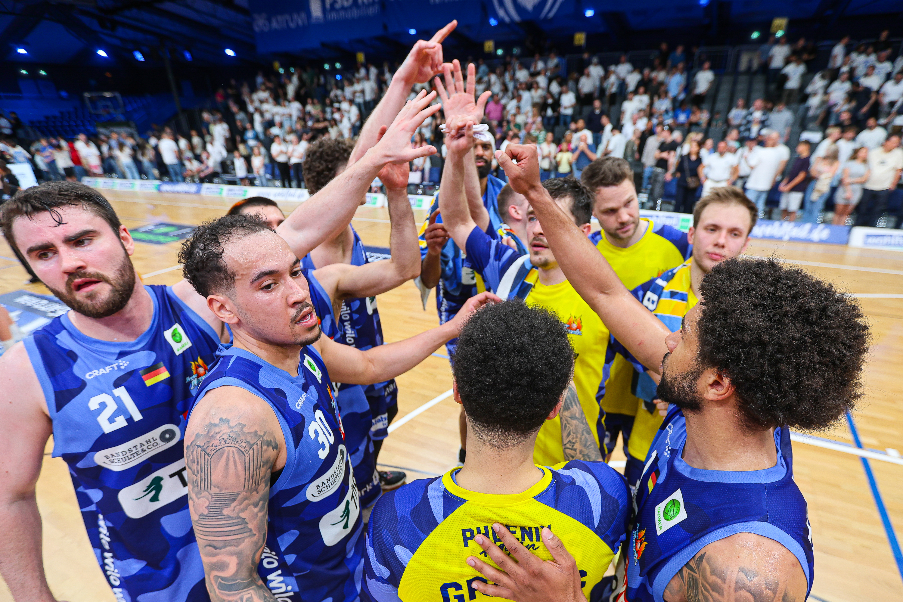 Mehrere Basketballspieler in blauen und gelben Trikots jubeln gemeinsam auf dem Spielfeld