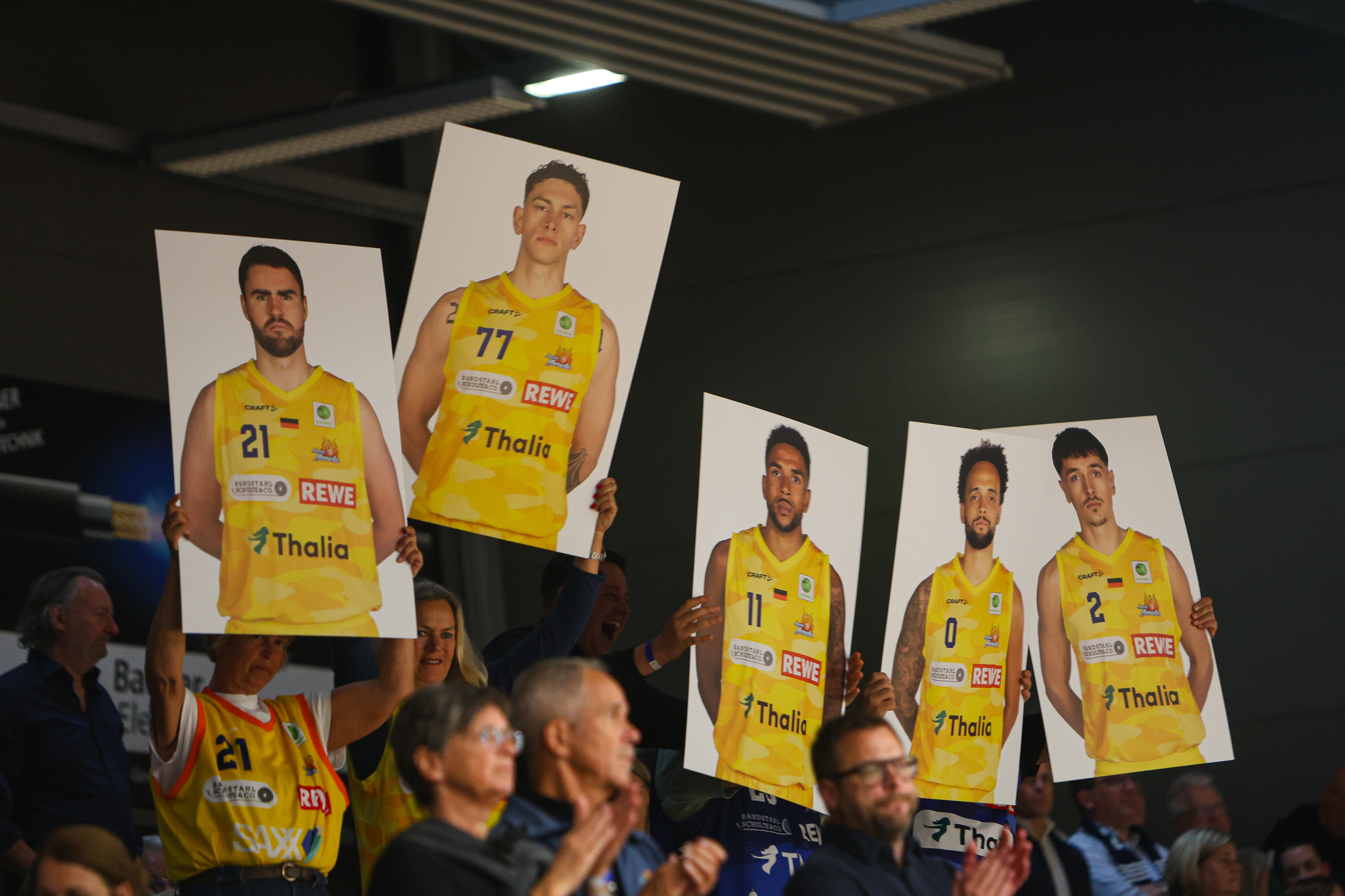Mehrere Fans halten gelbe Plakate mit Basketballspielern und jubeln voller Energie