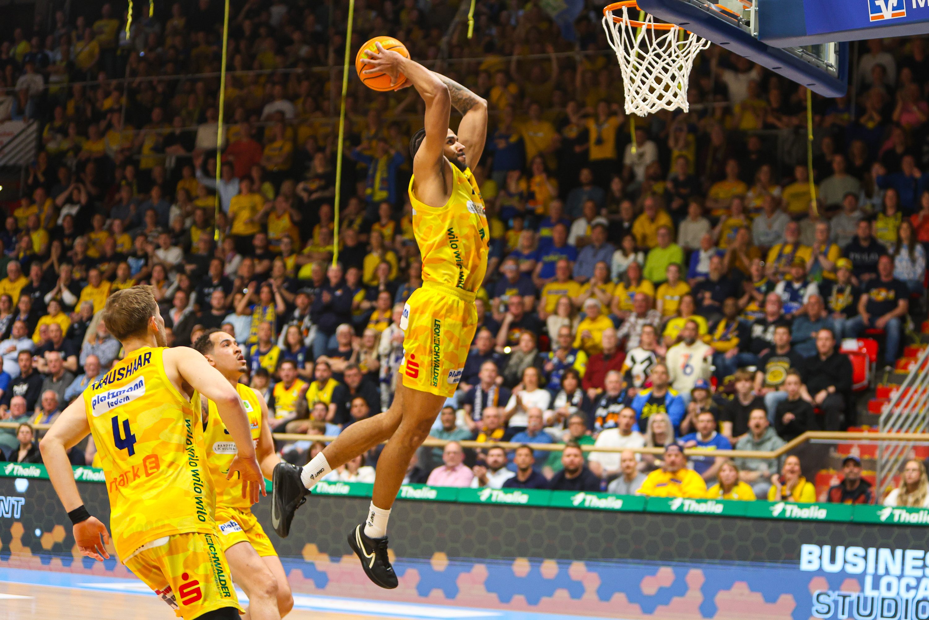 Ein Basketballspieler im gelben Trikot springt entschlossen zum Korb