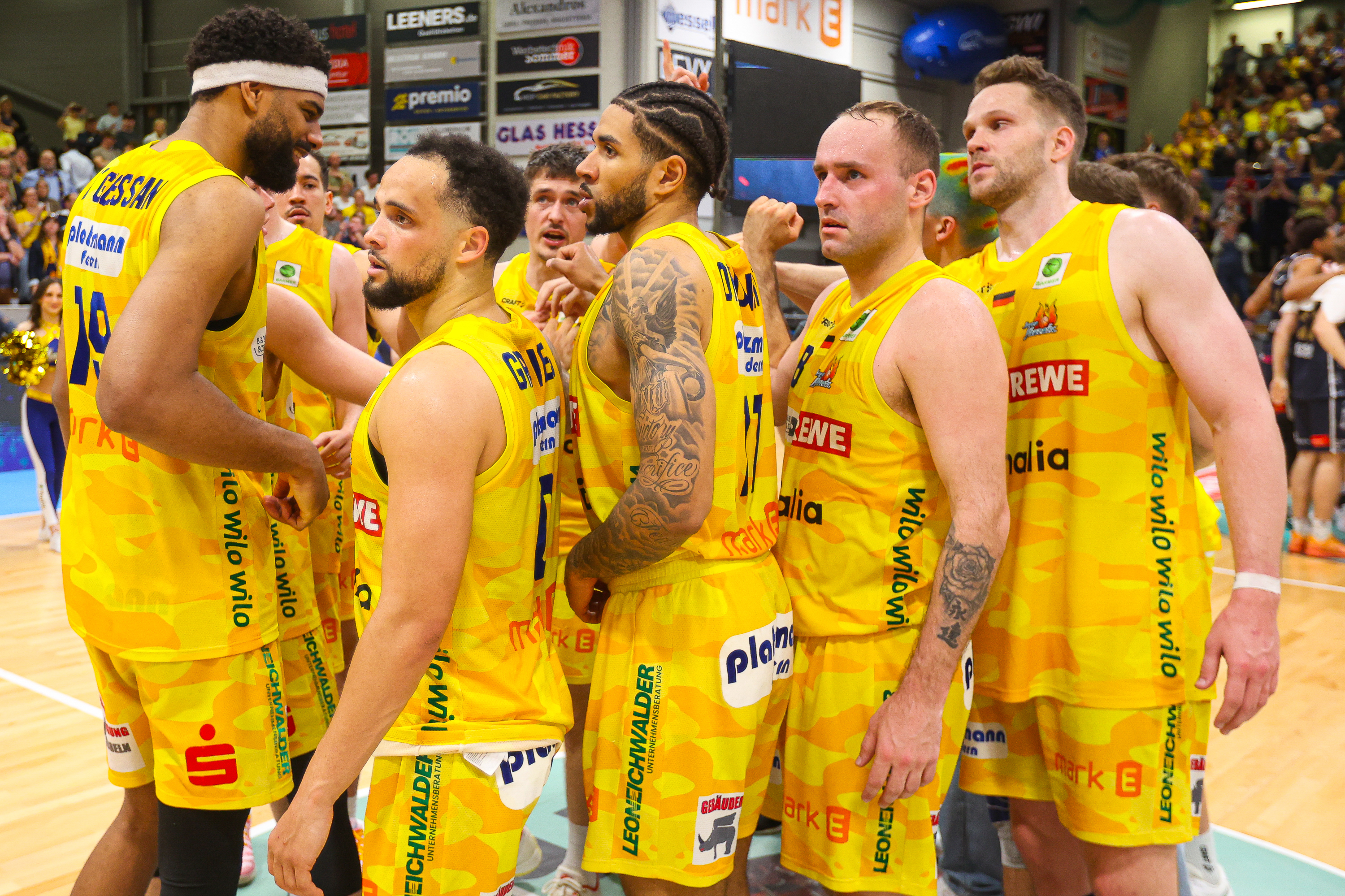 Eine Basketballmannschaft in gelben Trikots steht eng zusammen und blickt ernst