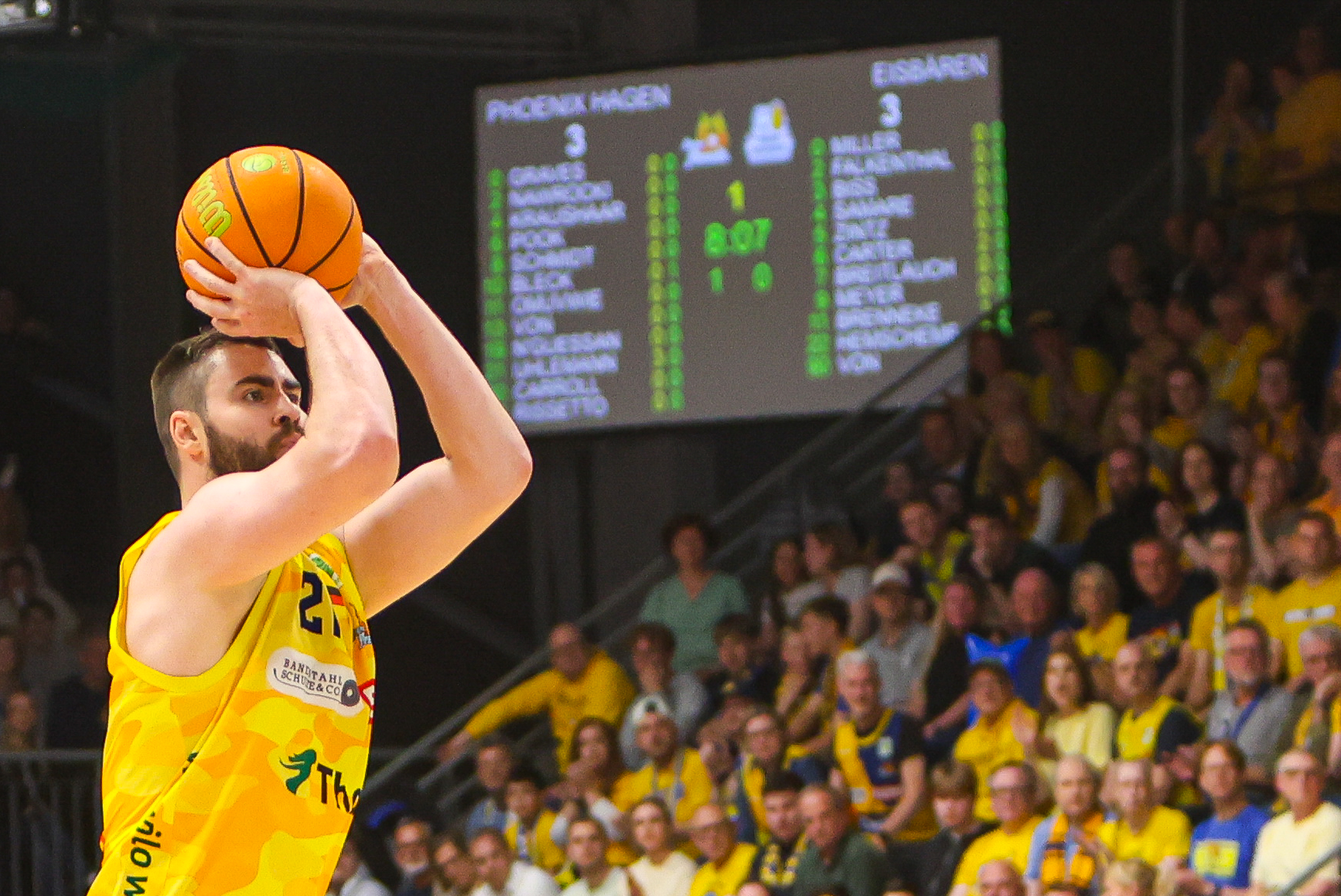 Ein konzentrierter Basketballspieler in gelbem Trikot wirft einen orangefarbenen Ball