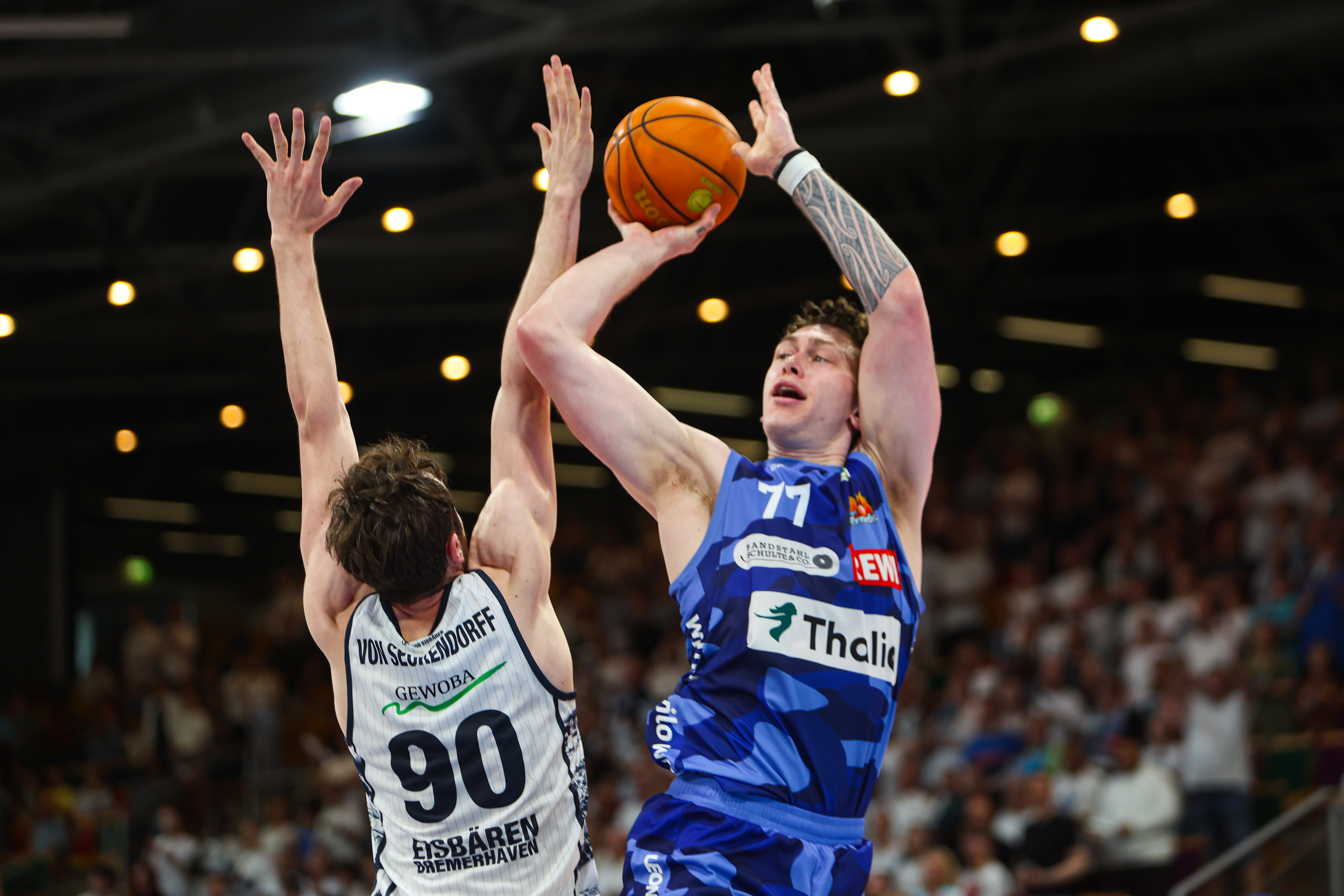 Zwei Basketballspieler im Spiel zeigen entschlossene Mienen und tragen blaue und weiße Trikots