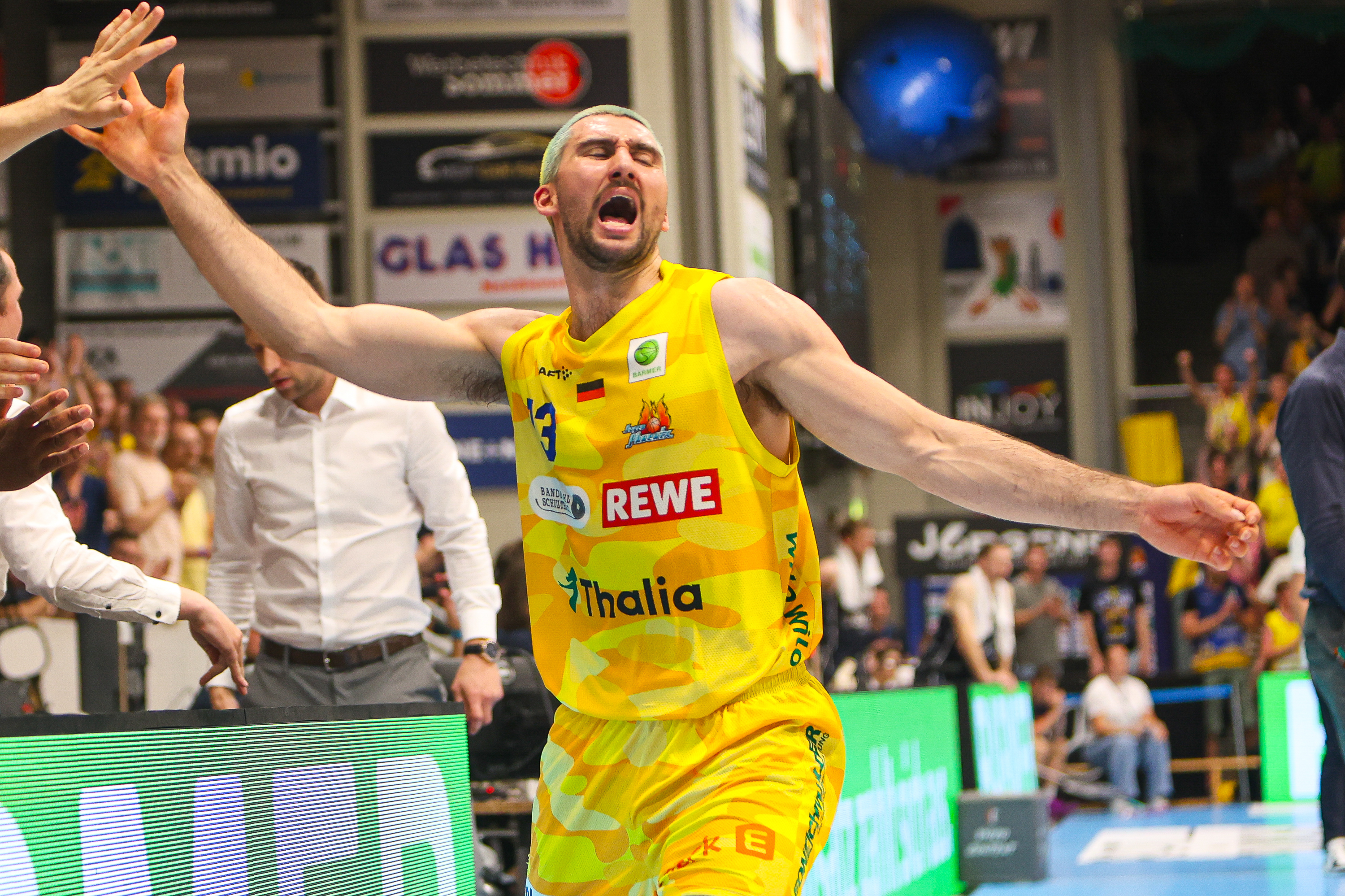 Lachender Basketballspieler in gelbem Trikot mit ausgebreiteten Armen in Halle