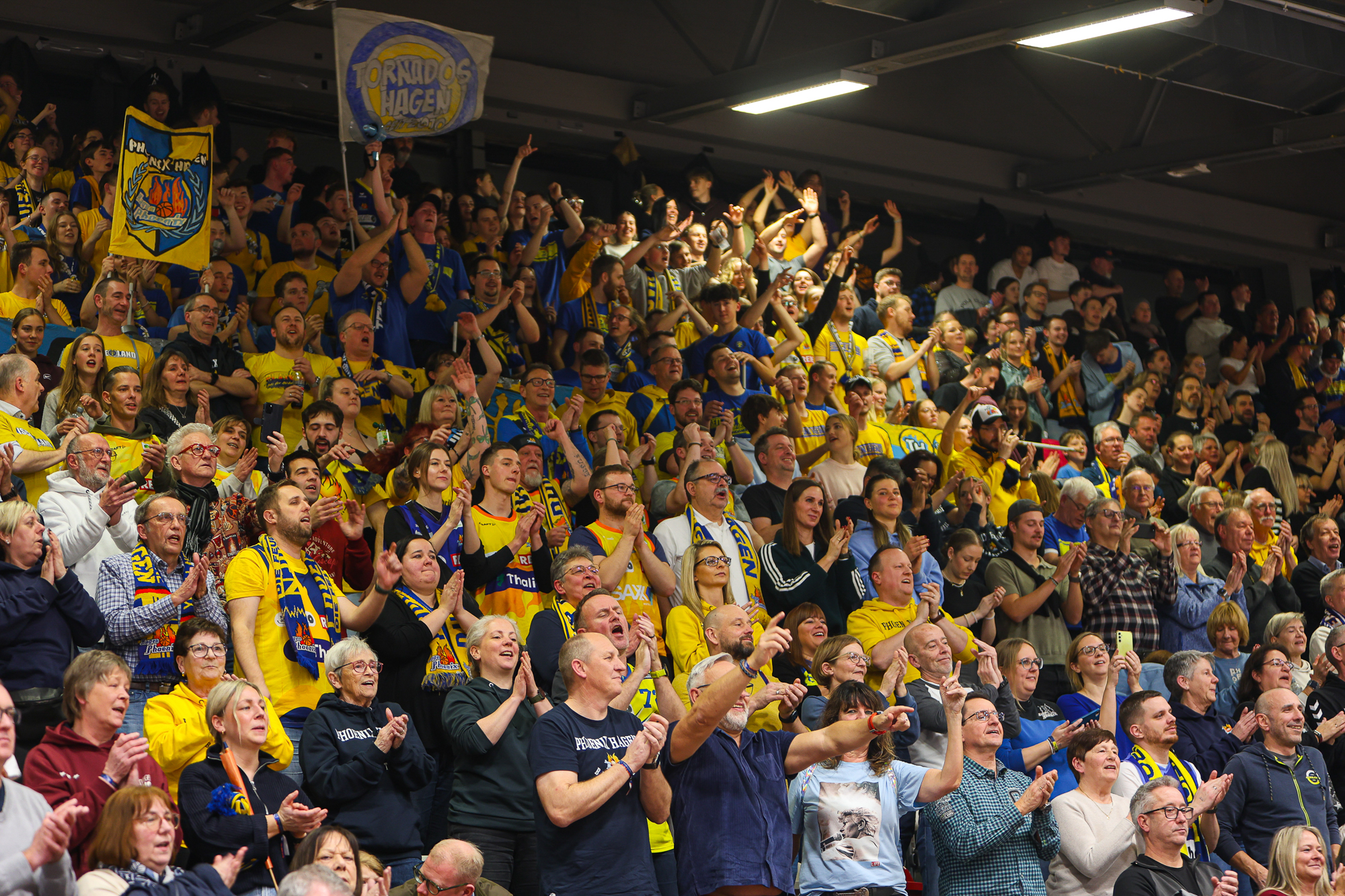 Viele fröhliche Fans in gelben Trikots jubeln gemeinsam in einer vollen Halle