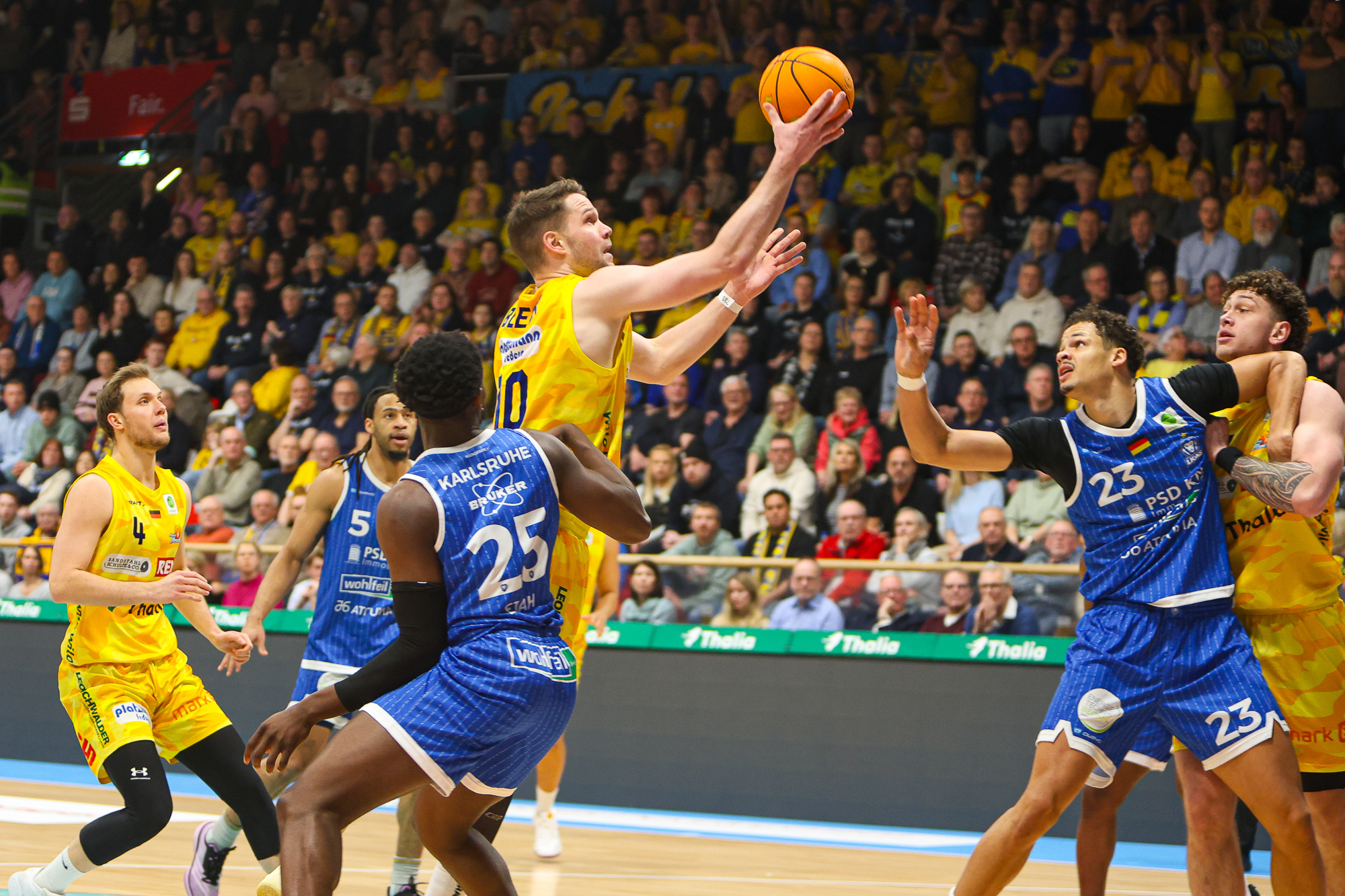 Mehrere Basketballspieler in gelben und blauen Trikots kämpfen dynamisch um den Ball