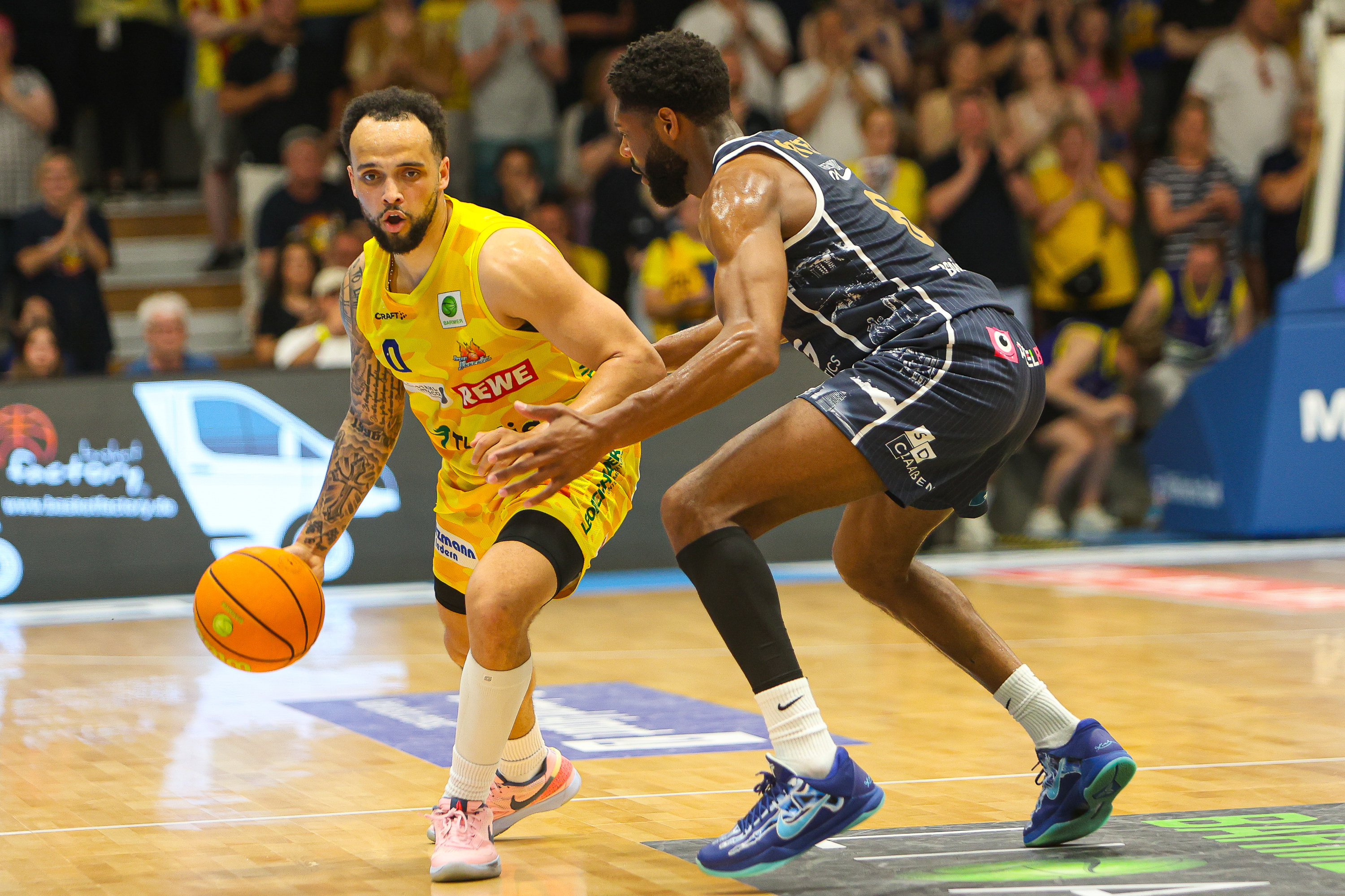 Zwei Basketballspieler konzentriert gelb gegen dunkelgrau mit Ball und Tattoos