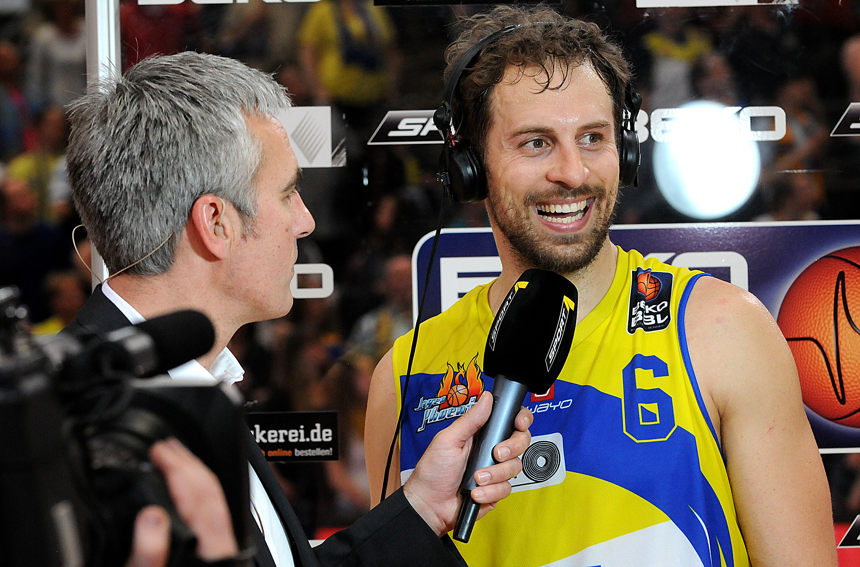 Ein Mann interviewt einen Basketballspieler im gelben Trikot mit konzentriertem Ausdruck