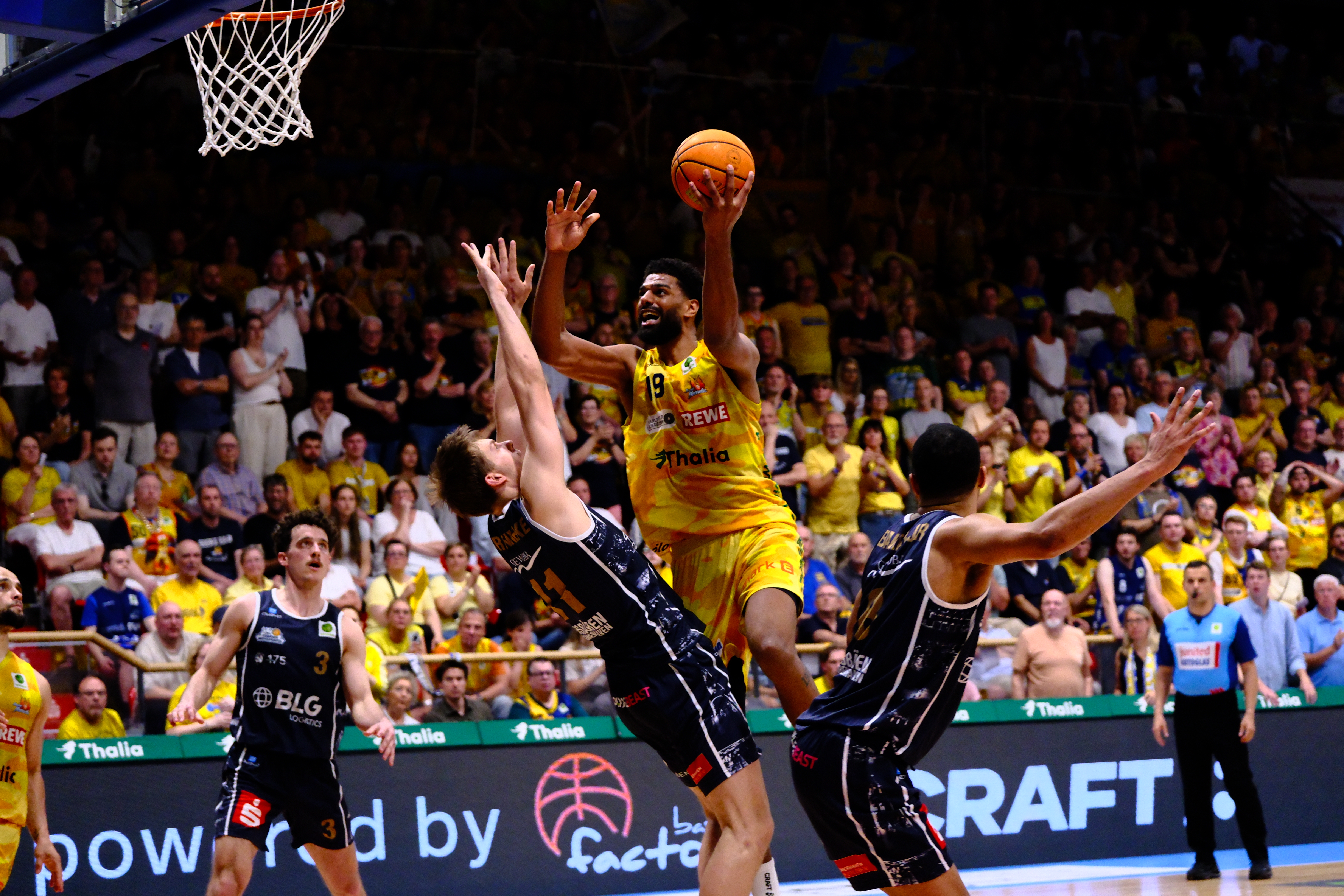 Fokussierter Basketballspieler in Gelb springt zum Korbleger, umringt von Blau