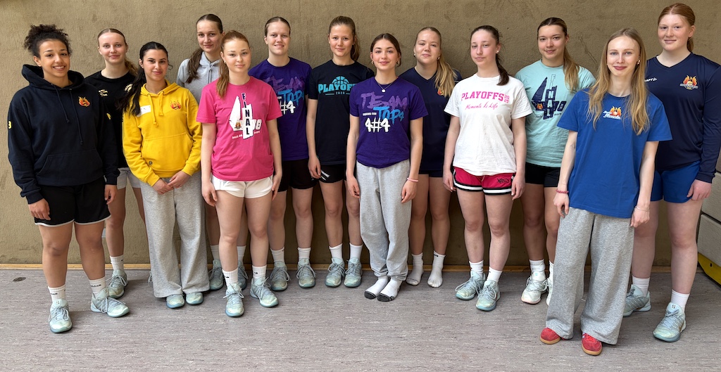 Vierzehn junge Frauen stehen lachend nebeneinander in Sportkleidung und bunten Shirts