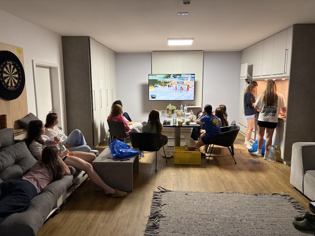 Eine Gruppe junger Menschen schaut entspannt ein Sportevent im Wohnzimmer auf dem Fernseher