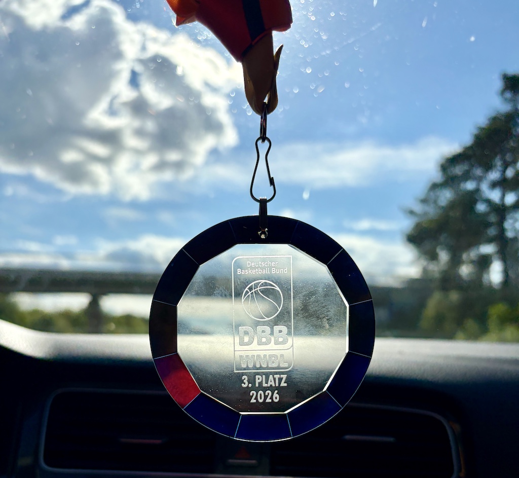 Eine silberne Basketballmedaille mit blauem Rand hängt am Rückspiegel des Autos