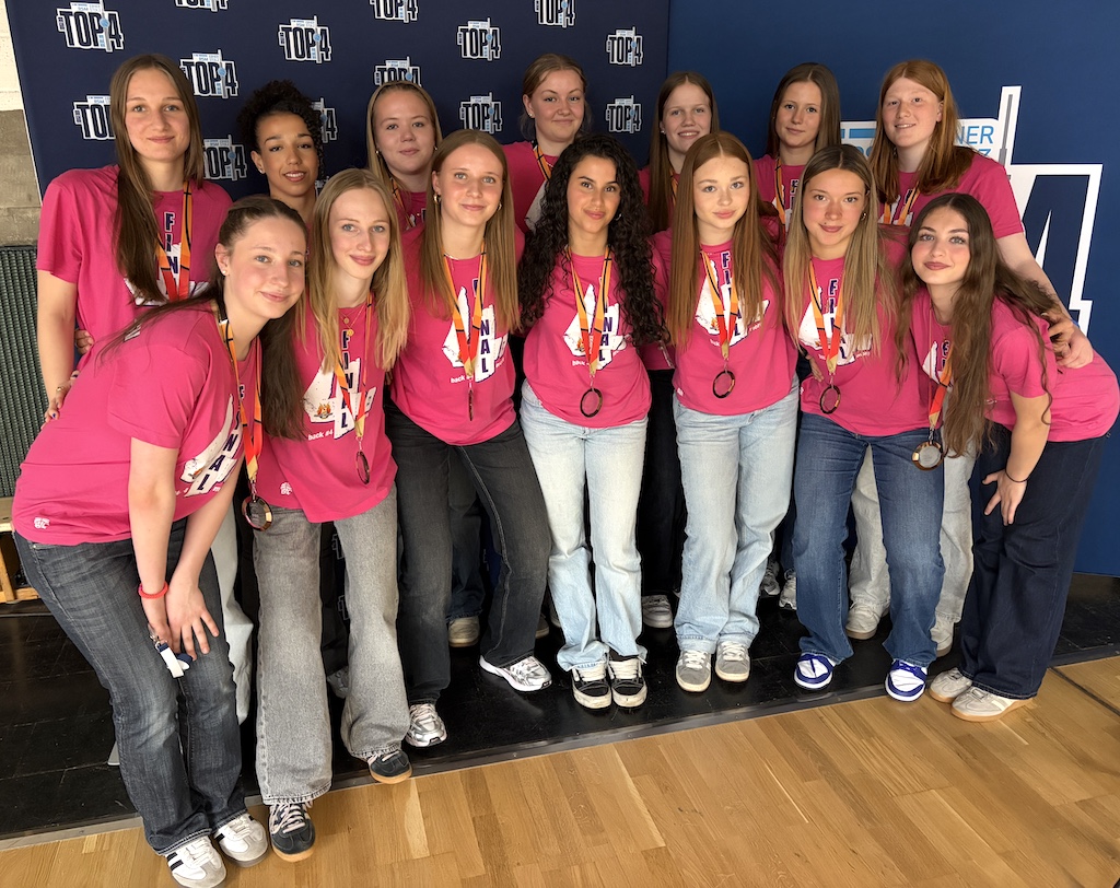 Eine Gruppe von Frauen lächelt, trägt pinke Shirts und Medaillen mit Jeans