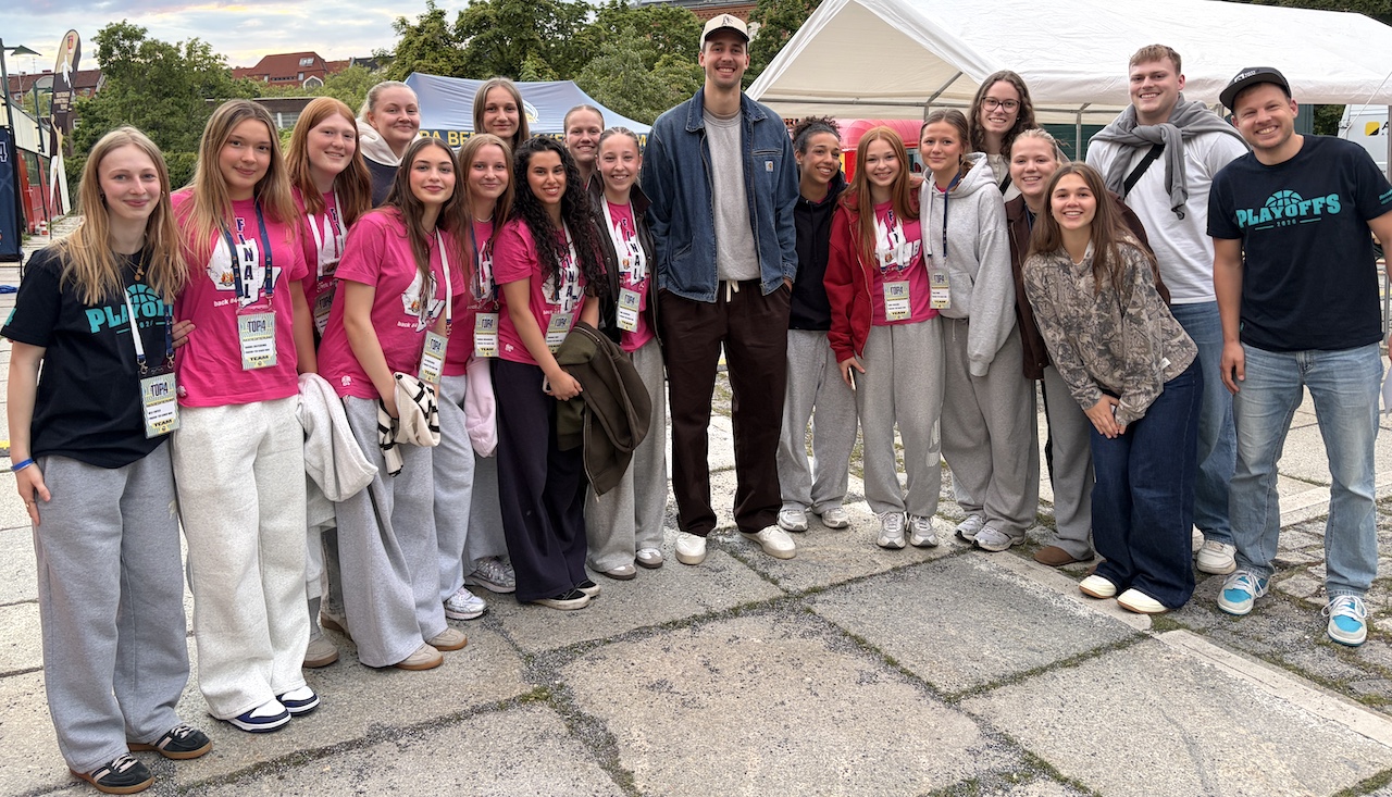 Eine Gruppe junger Menschen lächelt fröhlich, viele tragen pinke Shirts und Namensschilder