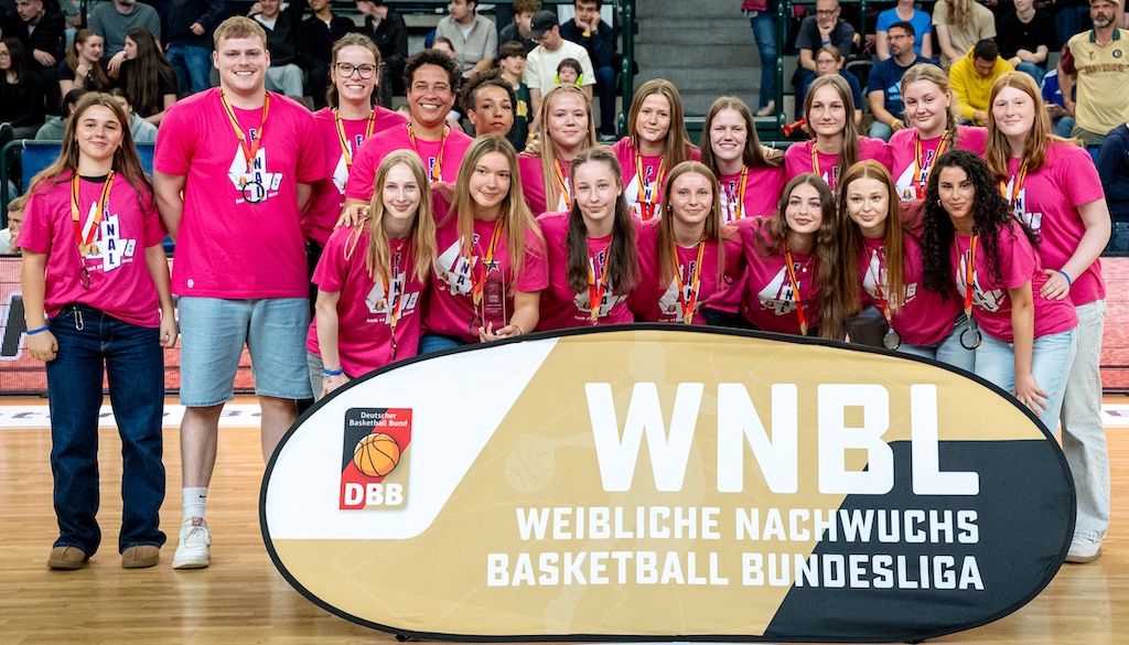 Eine Gruppe junger Frauen mit Medaillen und pinken T-Shirts lächelt stolz