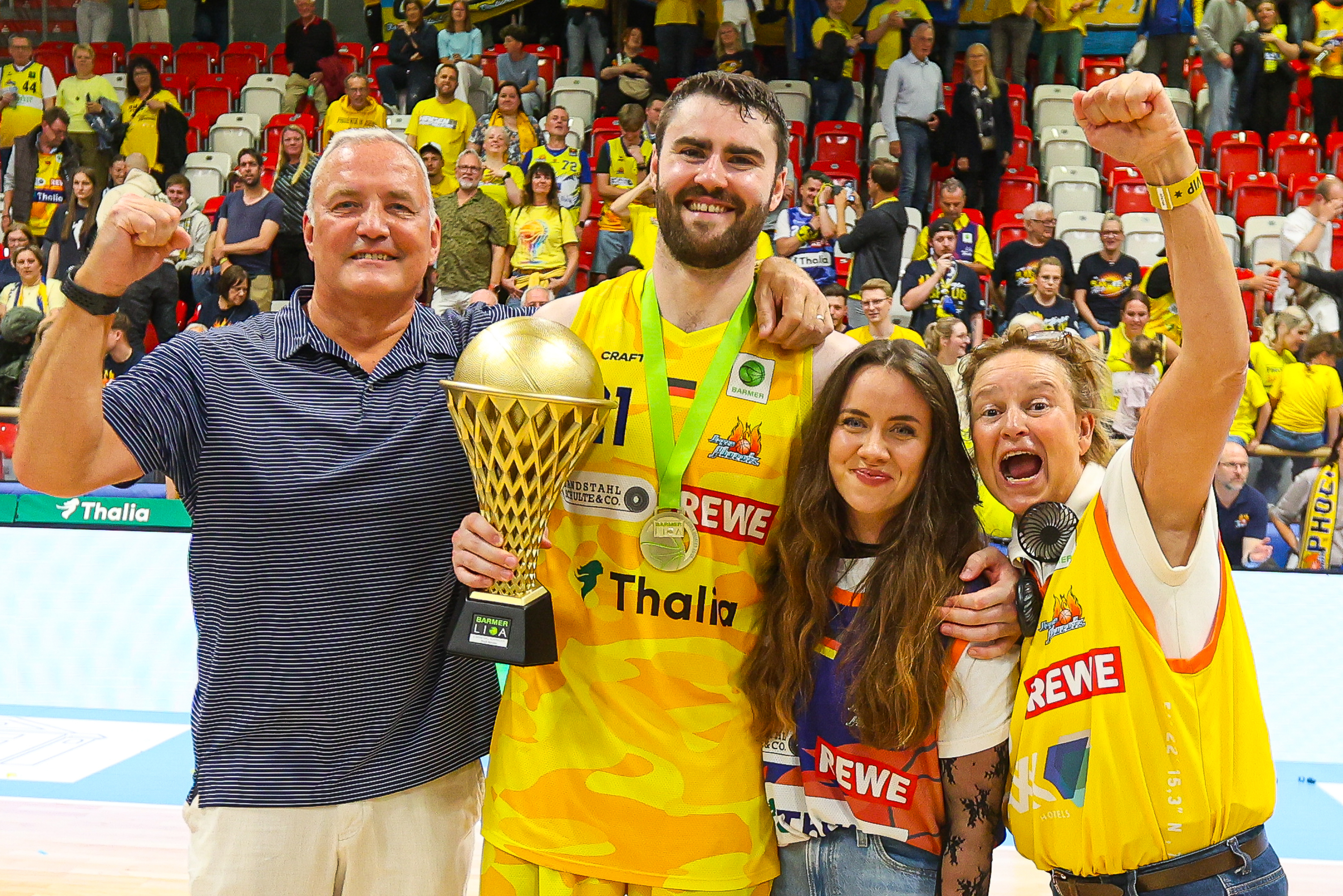 Vier jubelnde Personen in Gelb mit Pokal in einer Sporthalle