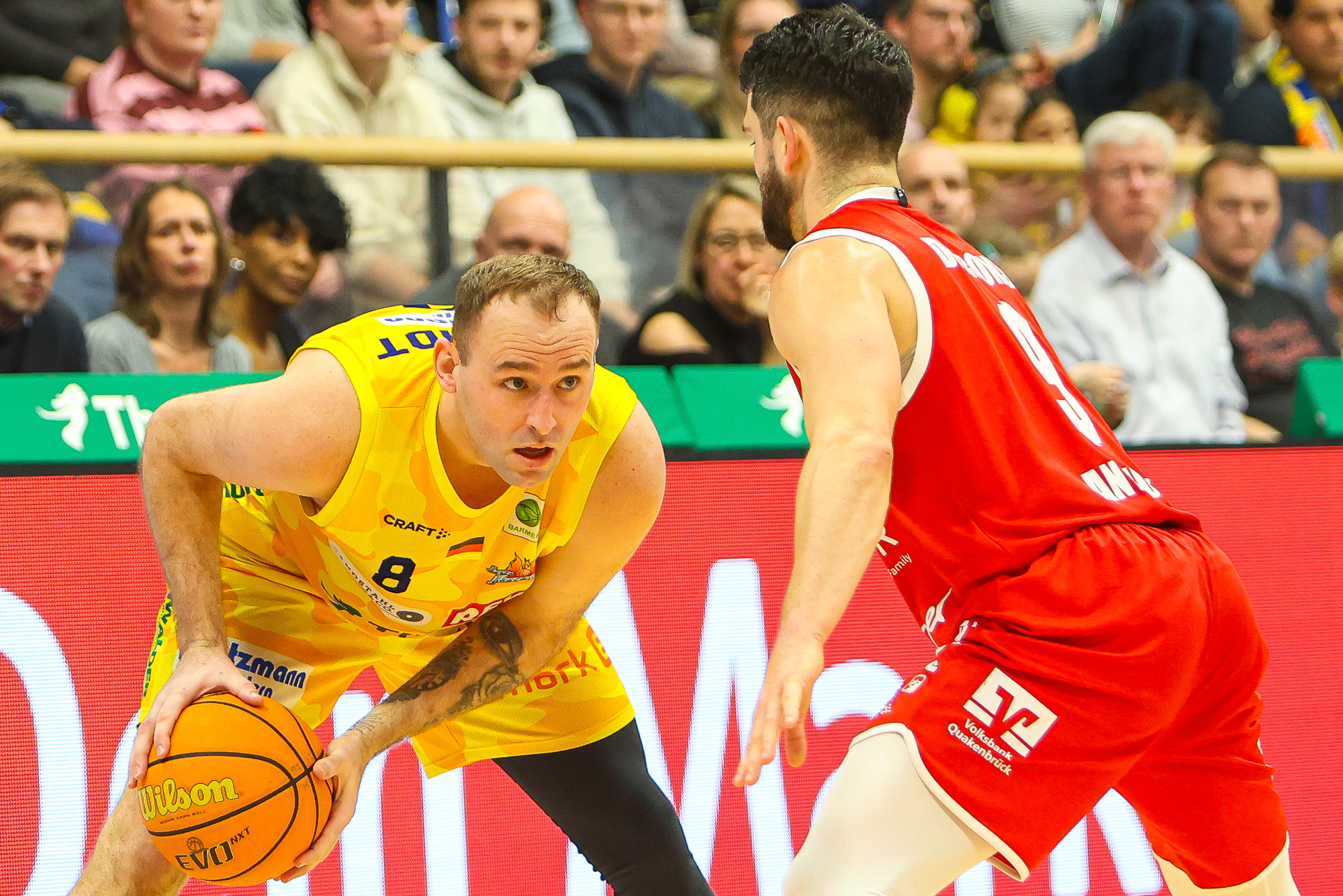 Konzentrierter Basketballspieler in Gelb dribbelt gegen Rotspieler, Halle bunt