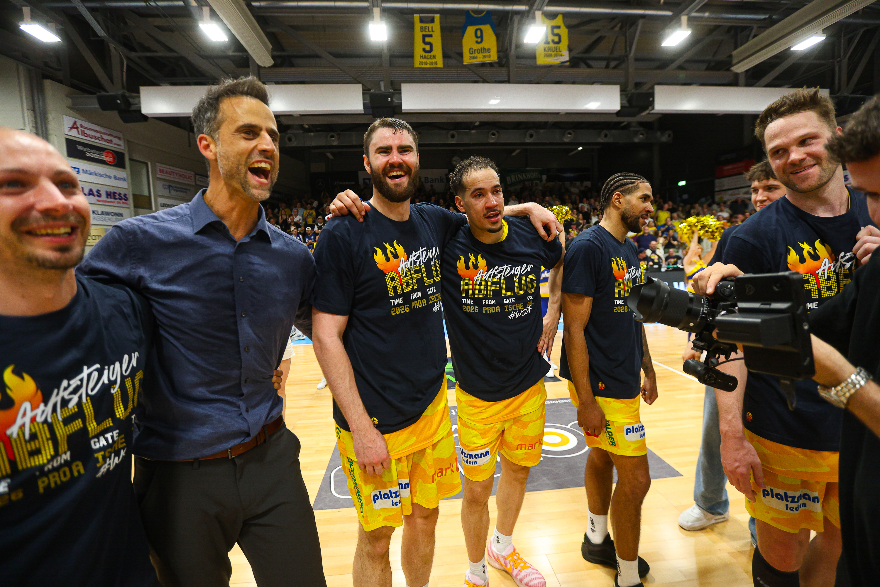 Jubelnde Basketballspieler in Blau Gelb mit Trainer und Kamera in Halle