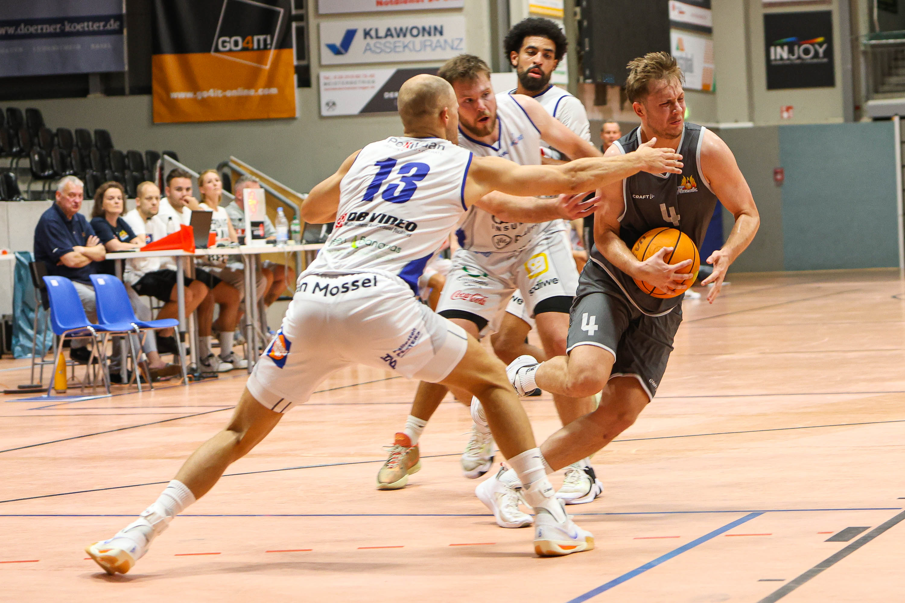 Drei fokussierte Basketballspieler in Grau und Weiss beim Dribbling, orangefarbener Ball