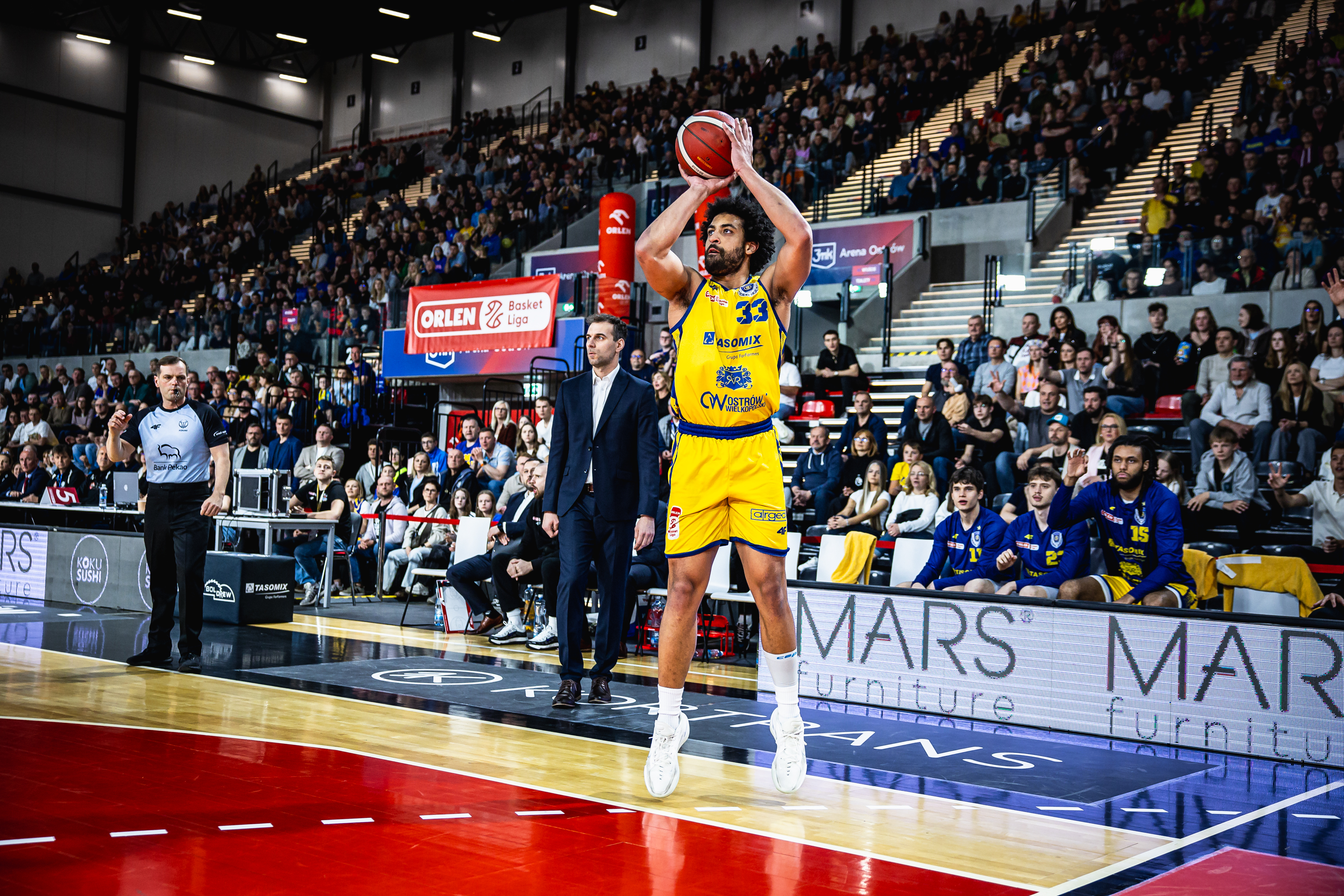 Konzentrierter Basketballspieler im gelben Trikot wirft roten Ball in voller Halle