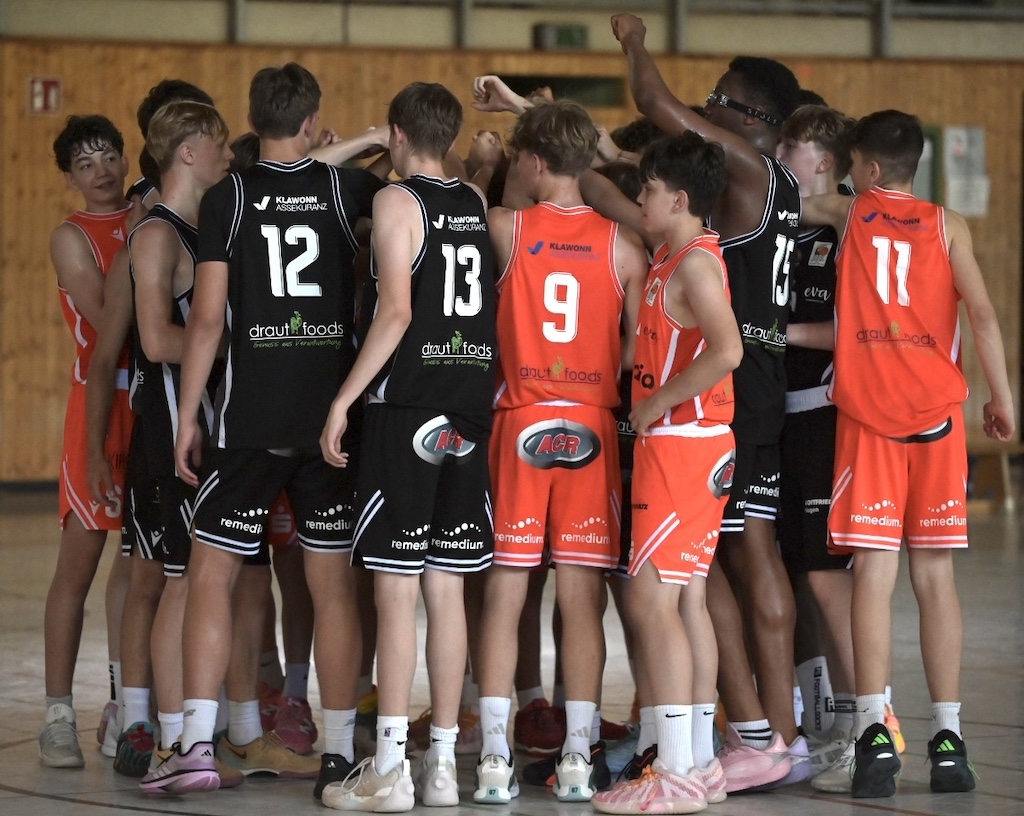 Jugendliche Basketballspieler in Schwarz und Orange jubeln im Kreis