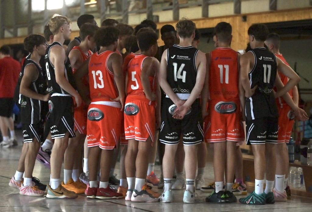Jugendliche Basketballspieler in Rot und Schwarz stehen konzentriert im Kreis in der Halle