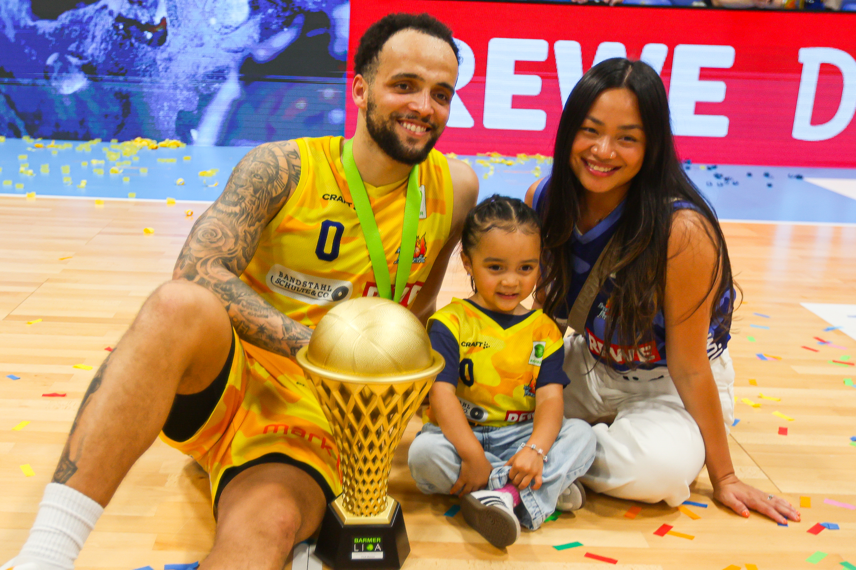 Lachendes Paar mit Kind und goldenem Pokal in gelben Trikots