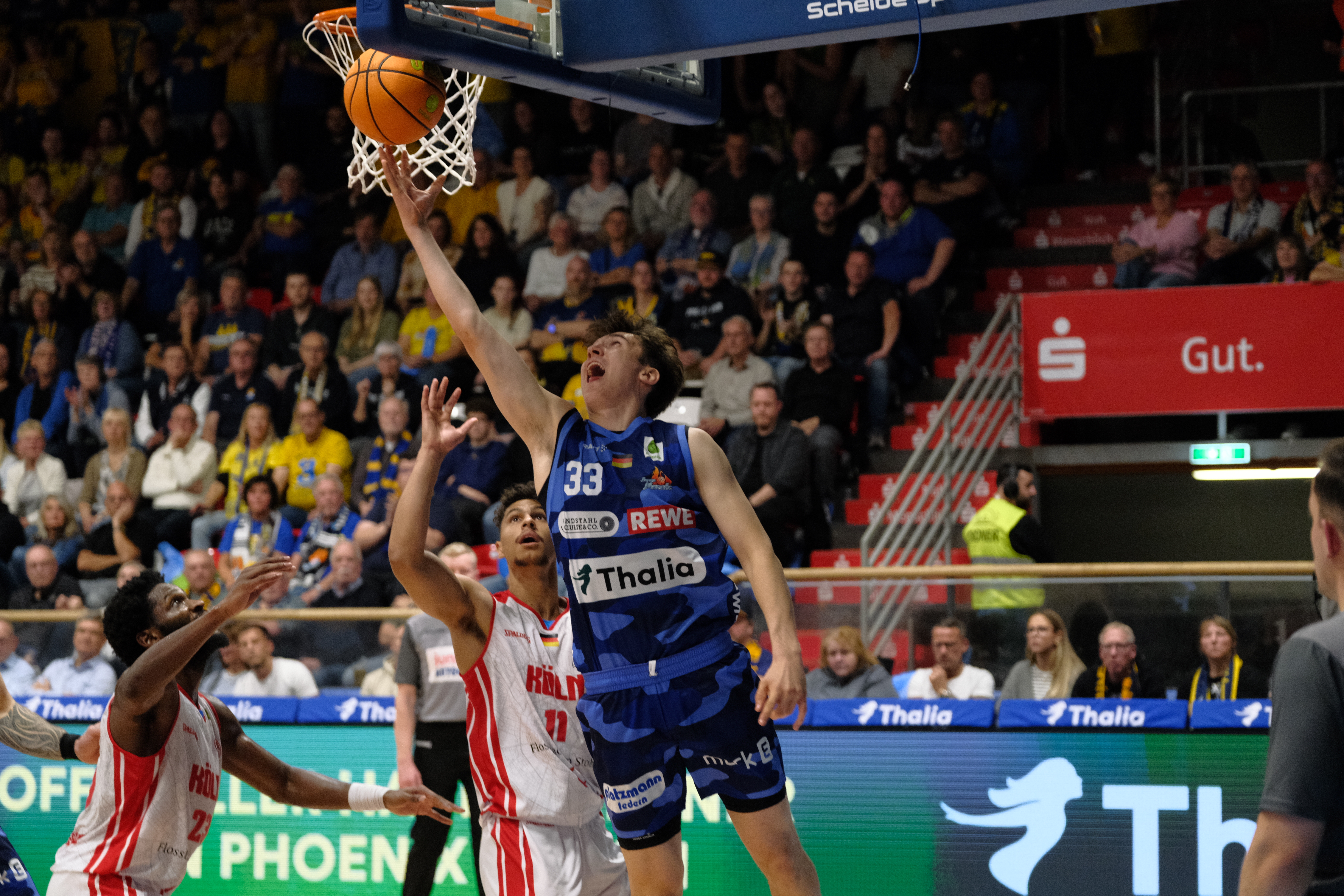 Jubelnder Basketballspieler in blau springt zum Korbleger im Stadion
