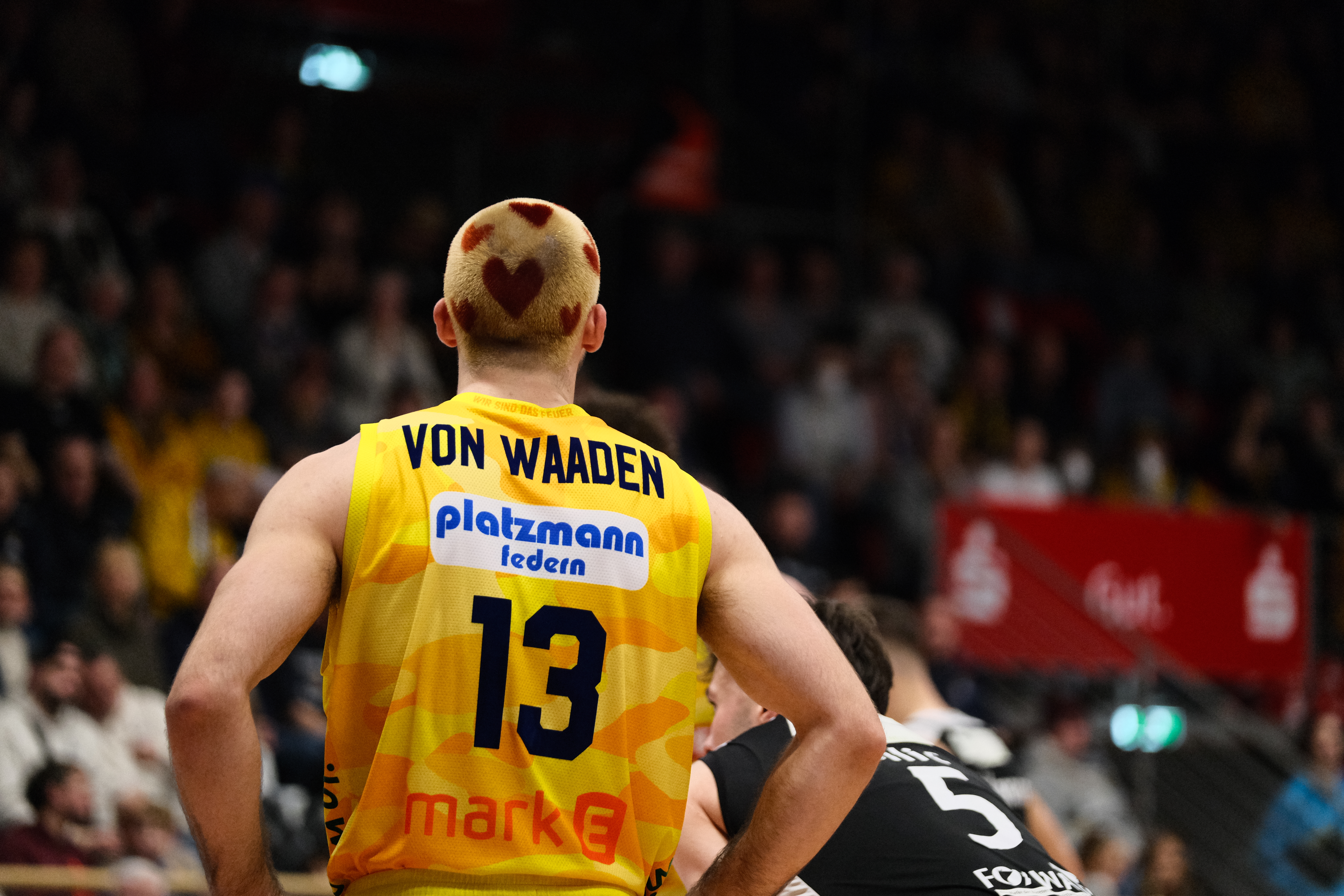 Basketballspieler mit neutralem Blick, gelbes Trikot, Herzmuster im Haar