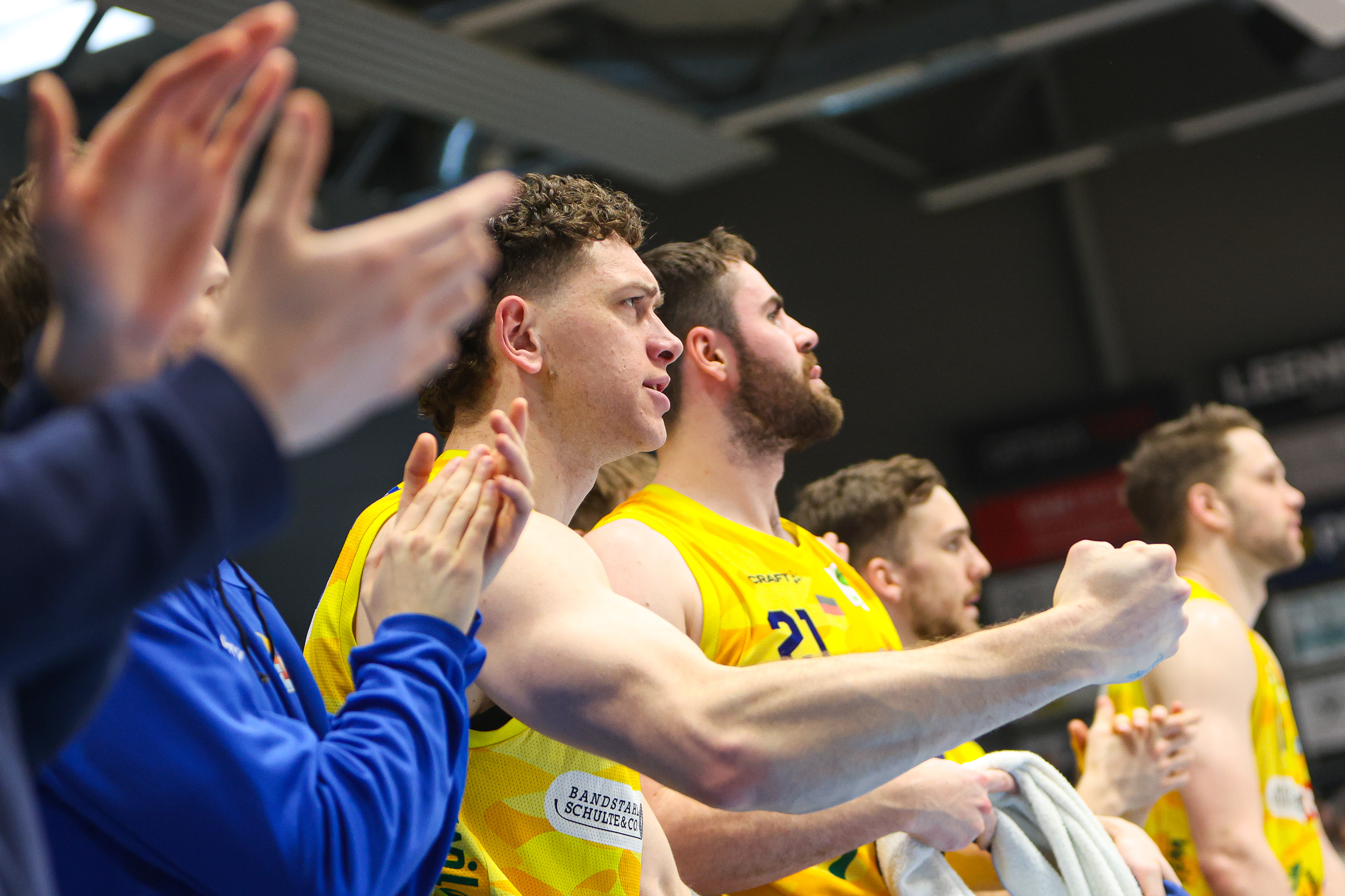 Applaudierende Basketballspieler in Gelb, fokussierter Blick, erhobene Faust