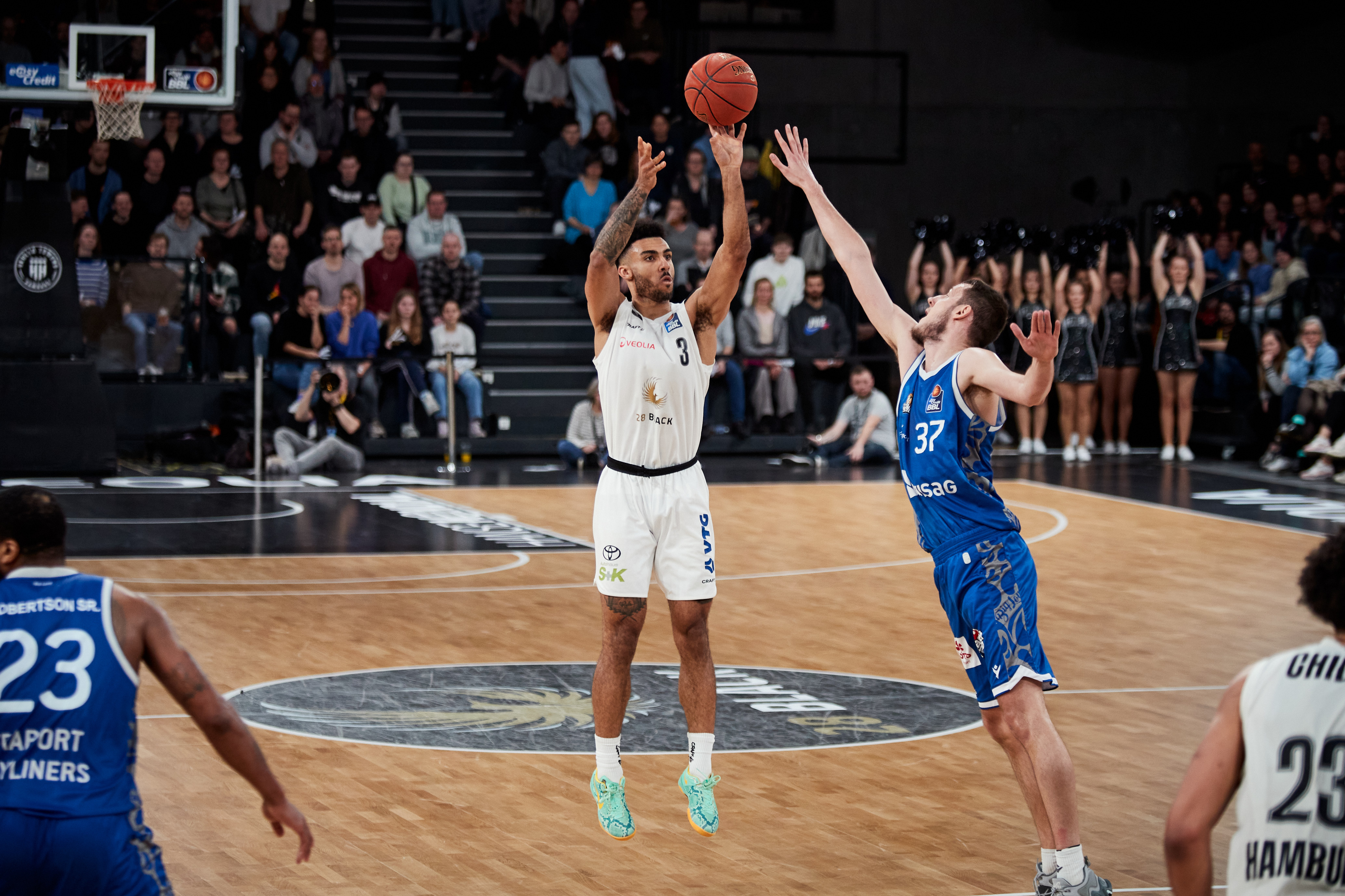 Konzentrierter Basketballspieler in Weiß wirft, Gegner in Blau blockt hoch
