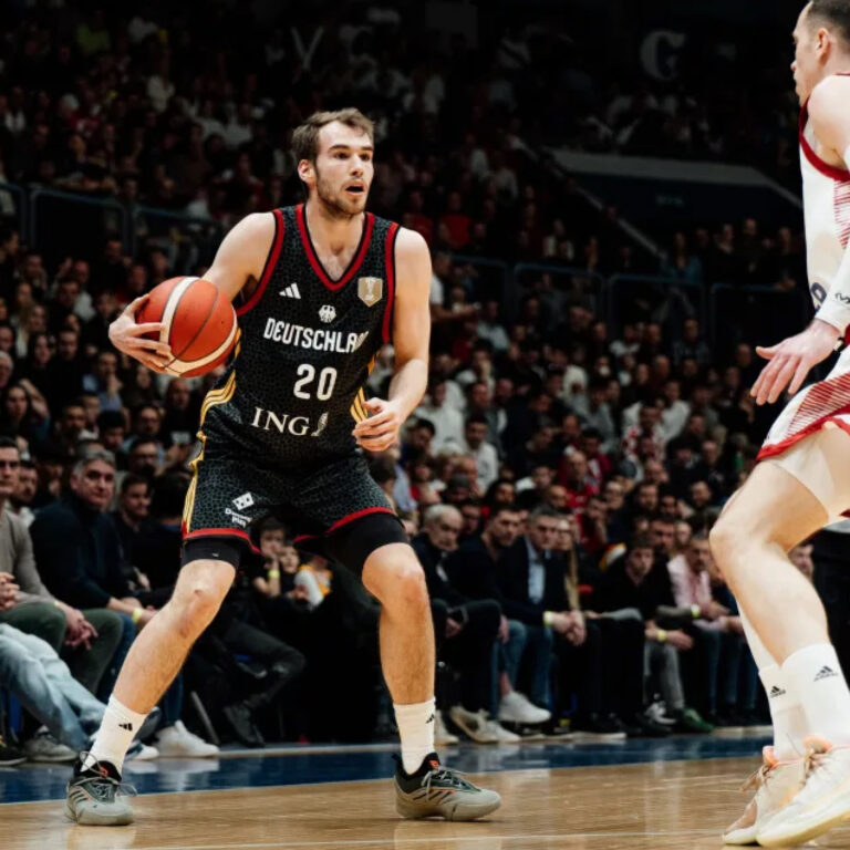 Fokussierter Basketballspieler im schwarzen Trikot dribbelt orangefarbenen Ball vor Publikum
