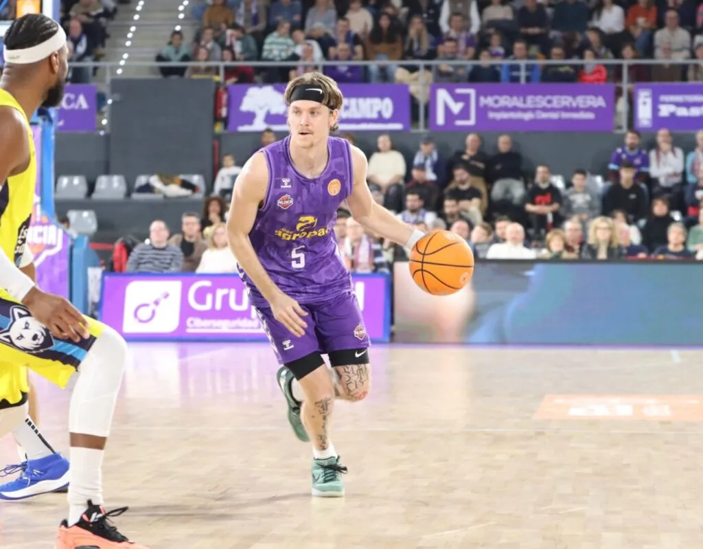 Fokussierter Basketballspieler in lila Trikot dribbelt orangen Ball, Stirnband