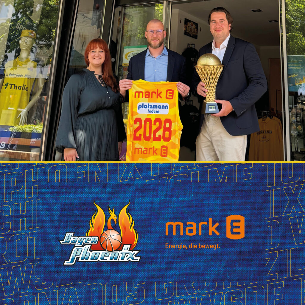 Drei lächelnde Personen mit gelbem Trikot 2028 und goldener Trophäe vor Glasfront