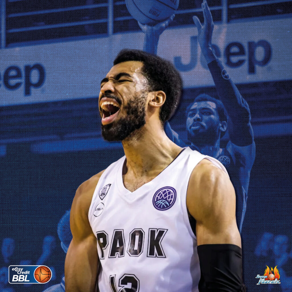 Jubelnder Basketballspieler im weissen PAOK Trikot vor blauem Hintergrund