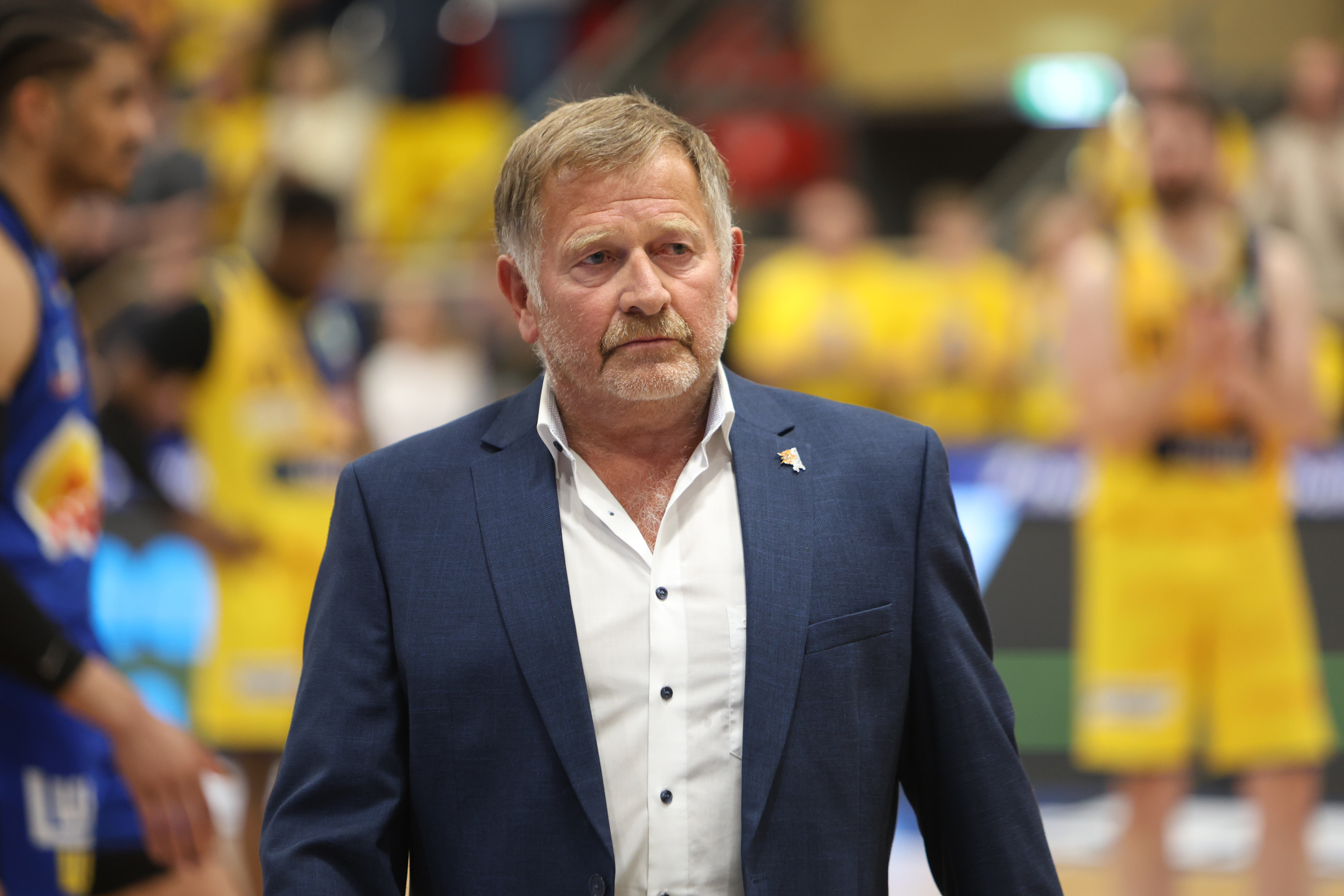 Ernster Mann im blauen Anzug, graues Haar, Sporthalle im Hintergrund