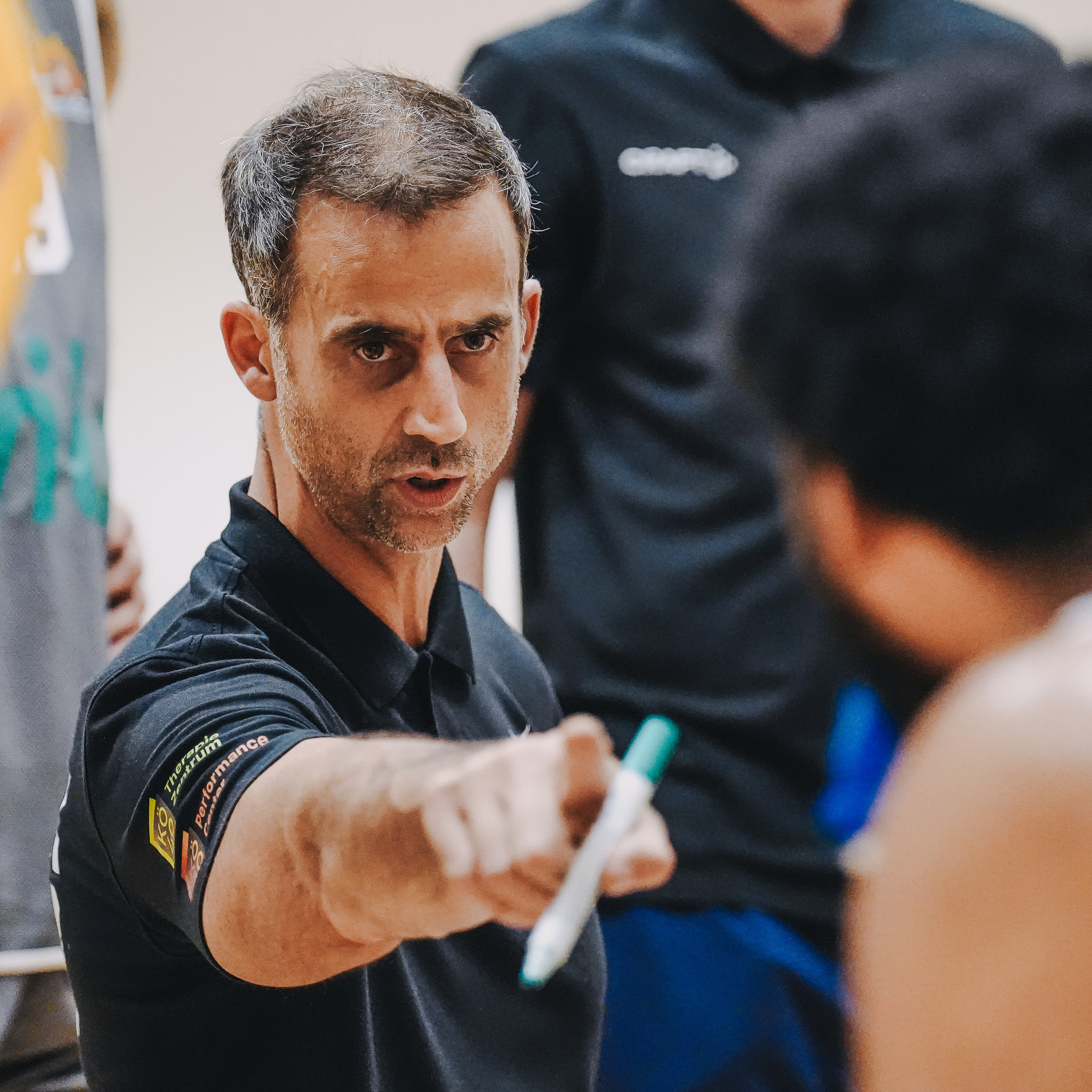 Ein Trainer im schwarzen Shirt gibt konzentriert mit einem Stift Anweisungen