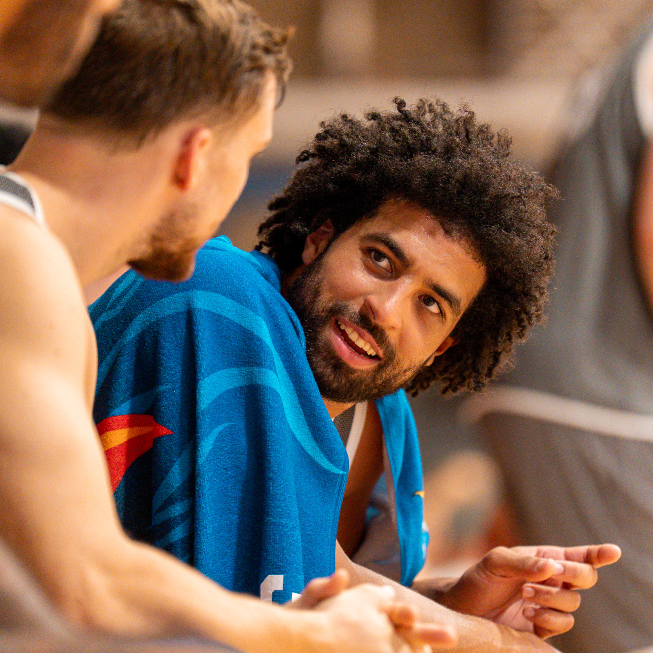 Laechelnder Basketballspieler mit lockigem Haar im blauen Trikot beim Gespraech