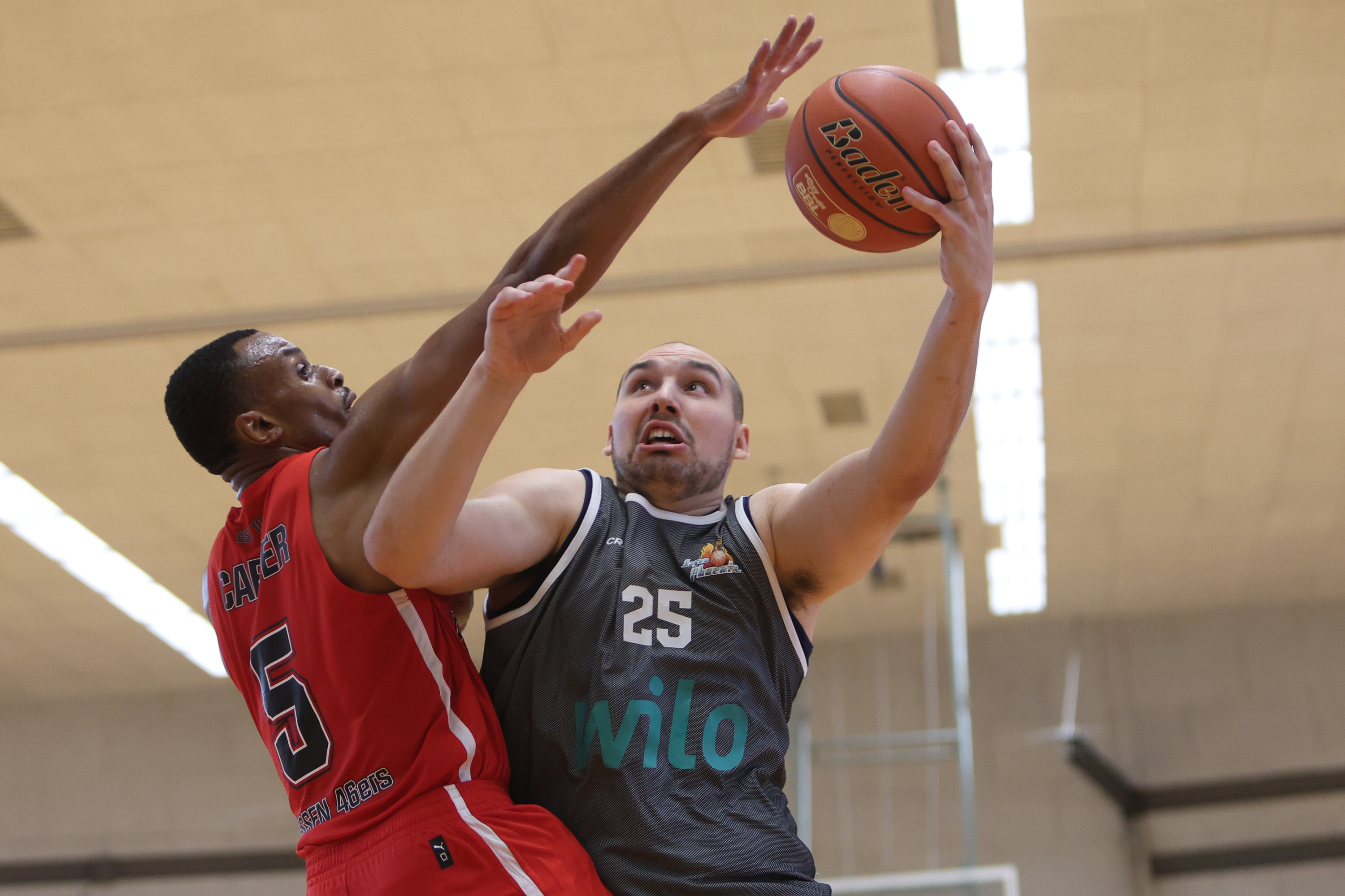 Basketballspieler in grauem Trikot beim Wurf gegen Verteidiger in Rot
