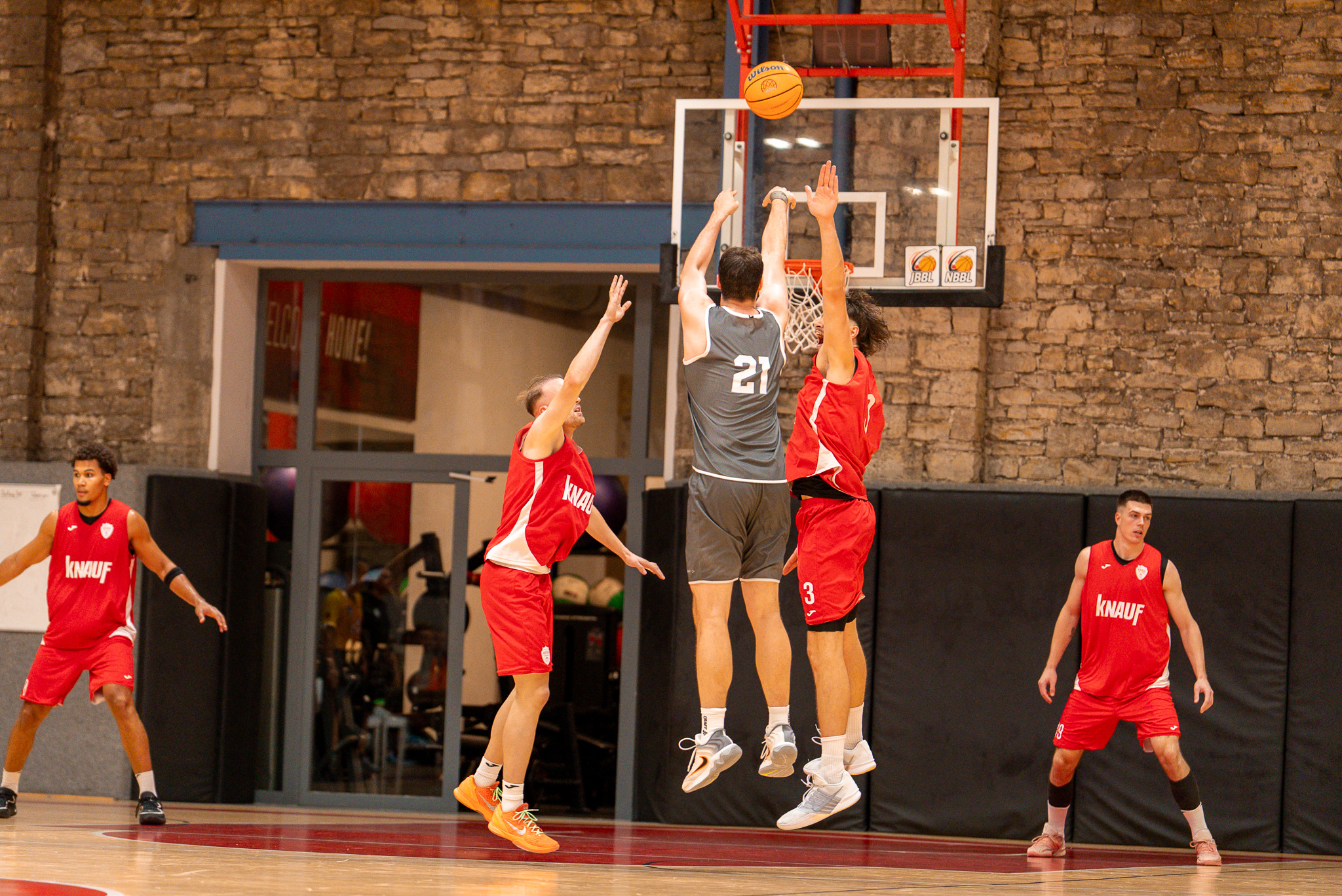 Basketballspieler in Grau wirft konzentriert den Ball gegen Gegner in Rot