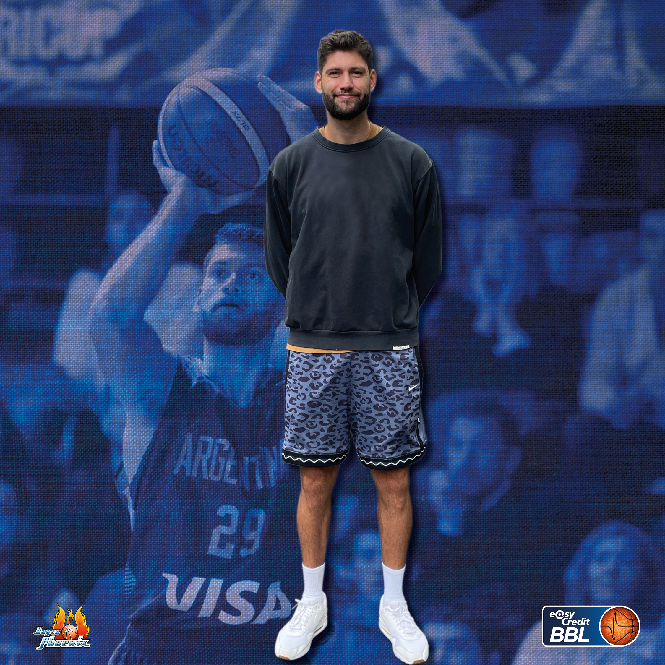 Laechelnder Mann mit Bart in grauem Pullover und Leopardenshorts vor blauem Hintergrund