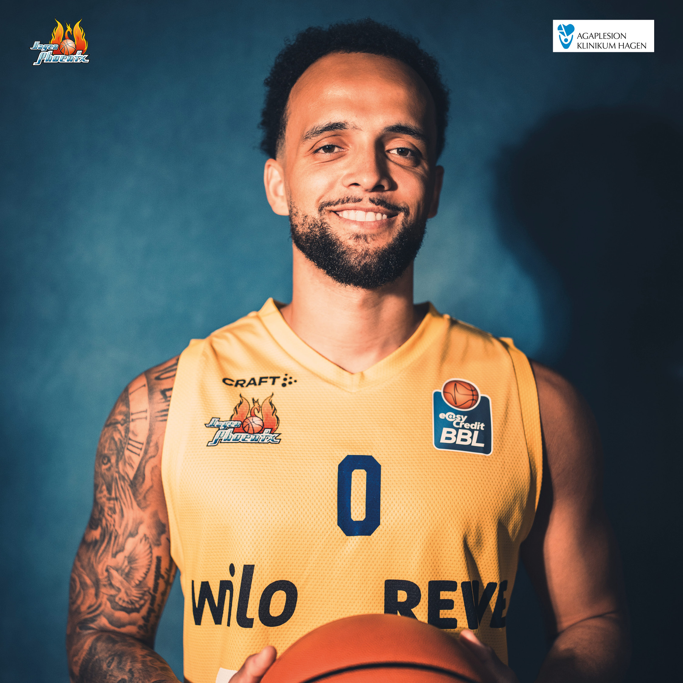 Laechelnder Basketballspieler im gelben Trikot mit Tattoos und Basketball