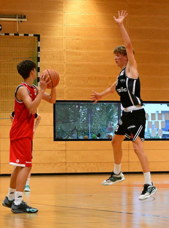 Zwei junge Basketballspieler in rot und schwarz kaempfen konzentriert um den Ball