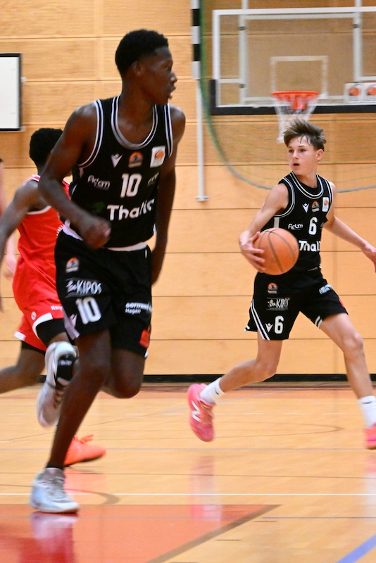 Zwei konzentrierte Basketballspieler in schwarzen Trikots beim Angriff in der Halle