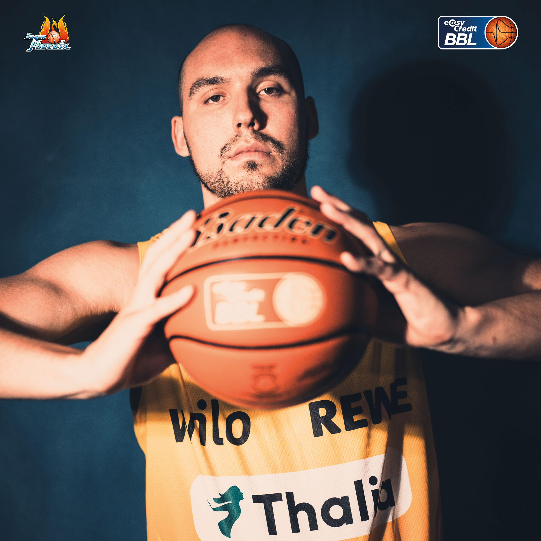 Ernst blickender Basketballspieler im gelben Trikot haelt einen Ball hoch
