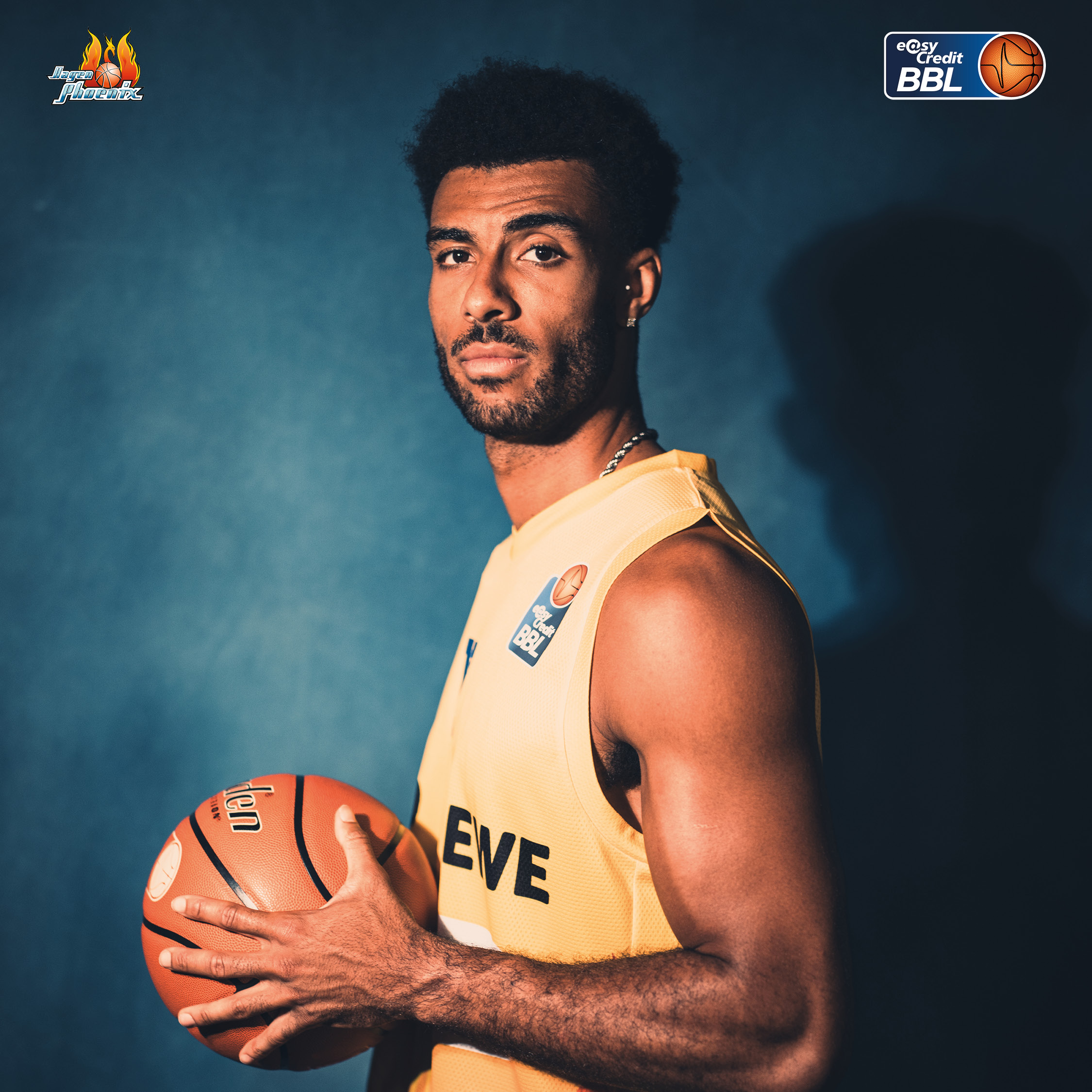Ein ernst blickender Basketballspieler im gelben Trikot haelt einen Ball