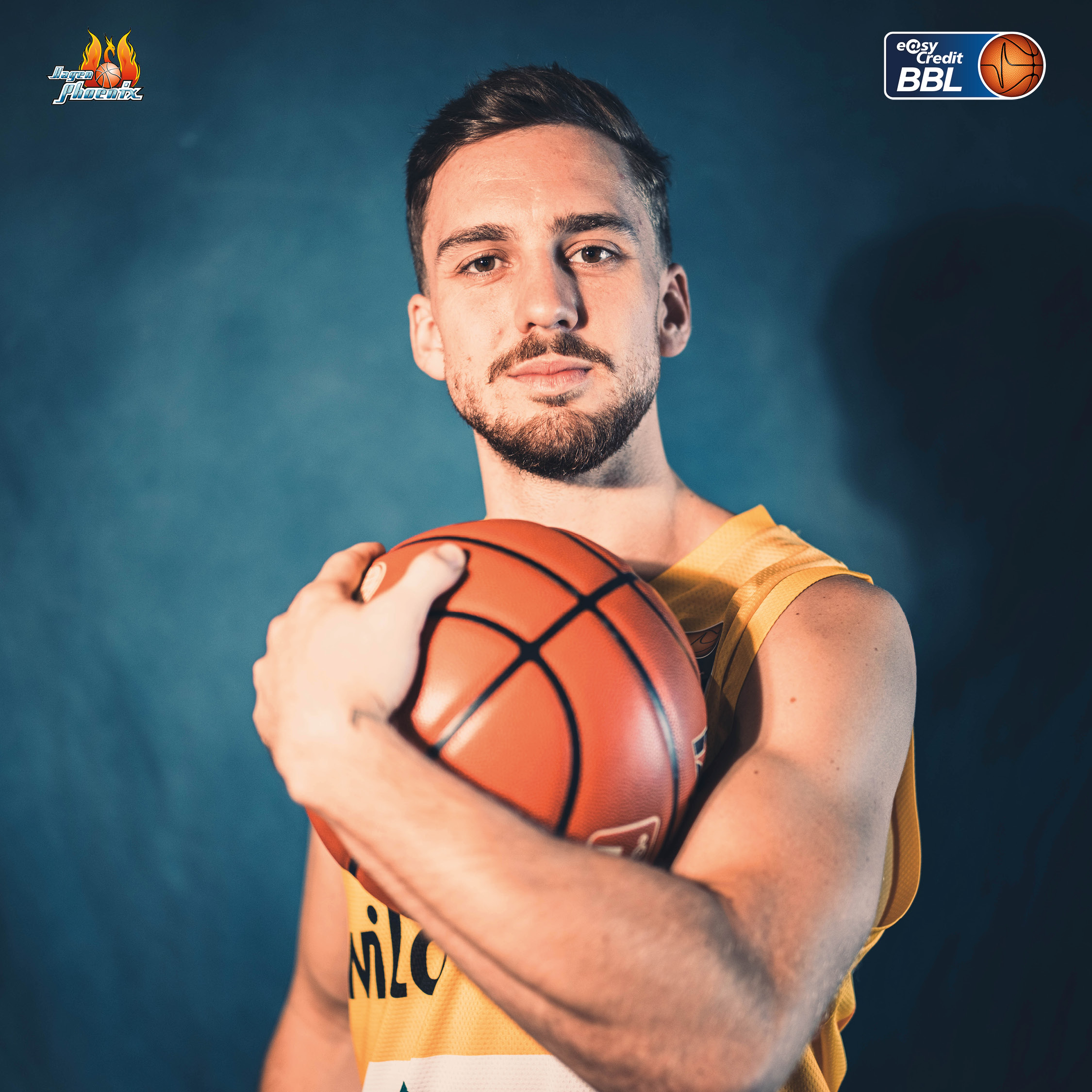 Ernst blickender Basketballspieler im gelben Trikot haelt einen Basketball